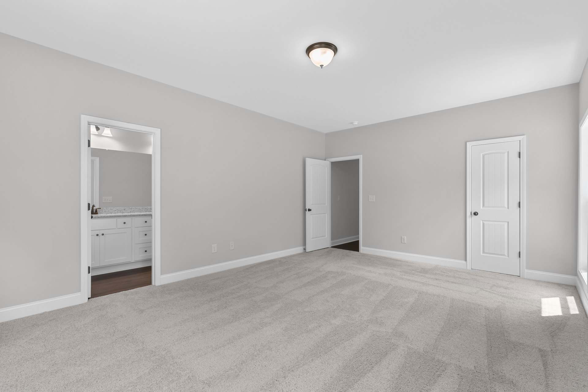 White-walled room with laminate flooring, white door featuring black handle, modern ceiling light fixture, and bathroom area with sink and white cabinets