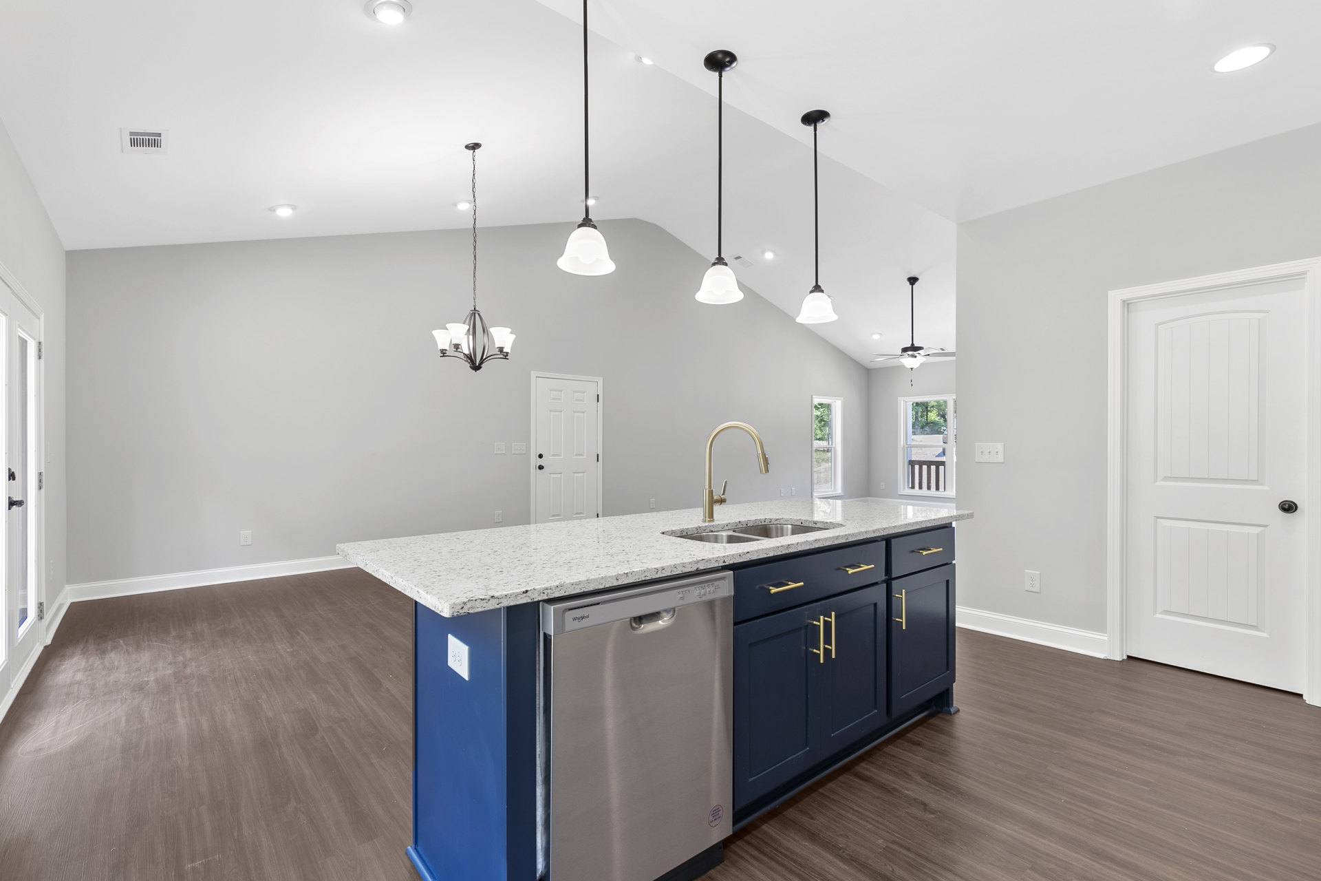 Stainless steel dishwasher beneath white quartz countertop, white shaker cabinets, undermount sink, black hardware, light wood flooring, white door with black handle, recessed