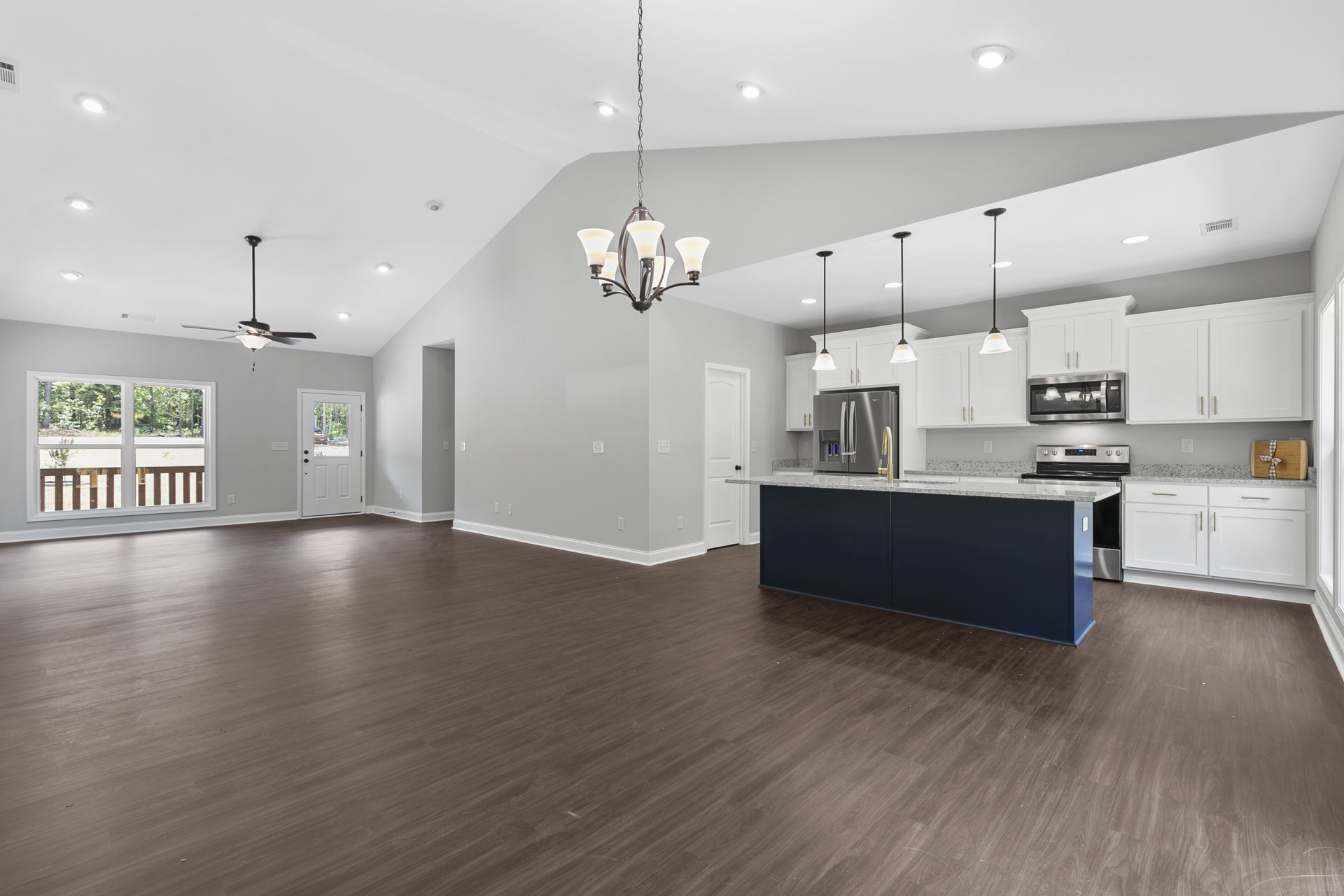 Spacious open-concept kitchen with wood flooring, central island featuring a sink, white cabinetry, stainless steel refrigerator, glass shelf with accent lighting, and a white door