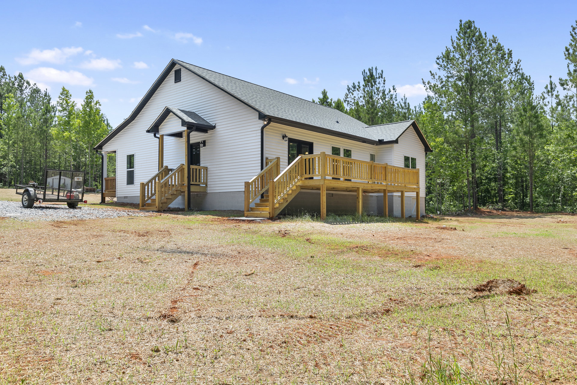 White house with wooden porch and stairs, surrounded by grass and trees, under partly cloudy sky