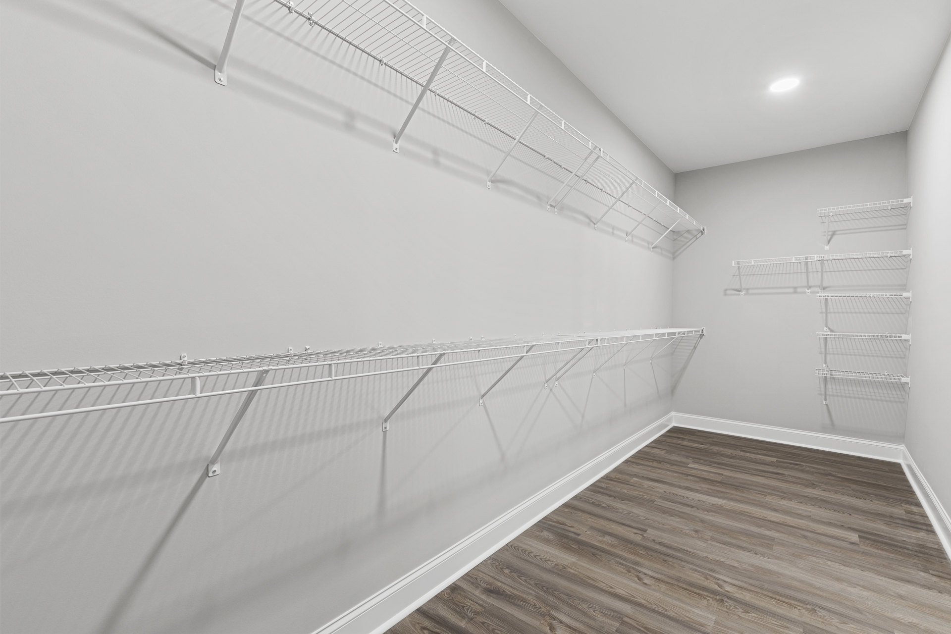 Wood floor and white plaster walls with built-in white shelves, recessed ceiling light, and staircase with wood handrail.
