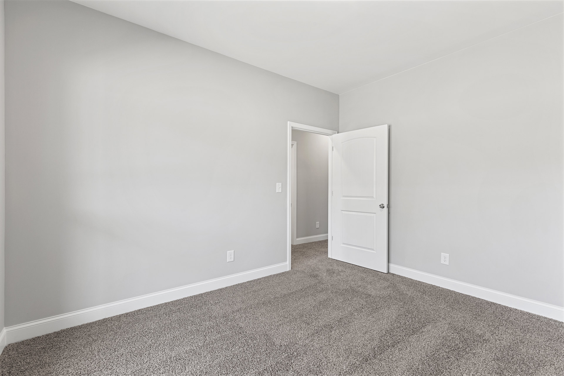 White paneled door with silver knob open to carpeted room, white walls and ceiling, simple white door frame