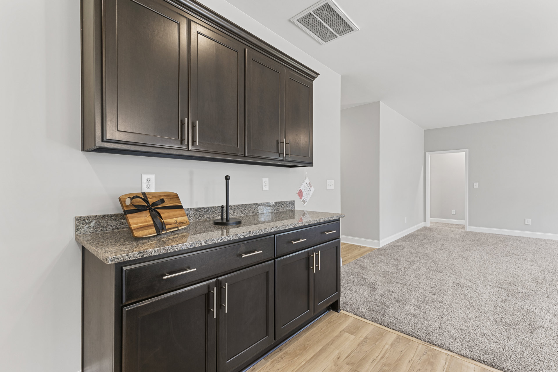 Kitchen with matte dark cabinets, granite countertops, wood cutting board, black pendant lamp, stainless steel sink, and ceiling vent