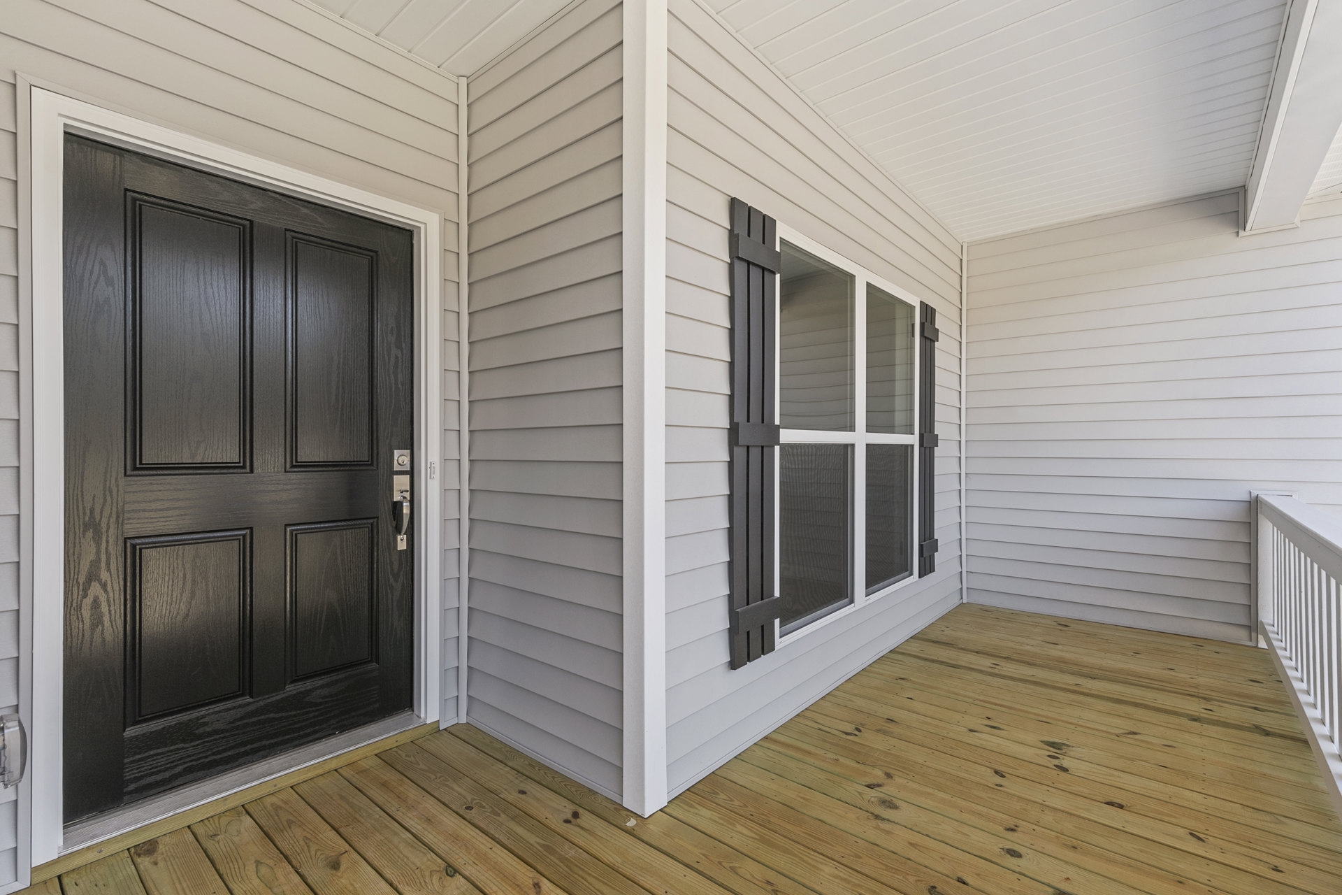 White front porch with black wood siding, black door with silver handle, white railing, and adjacent window