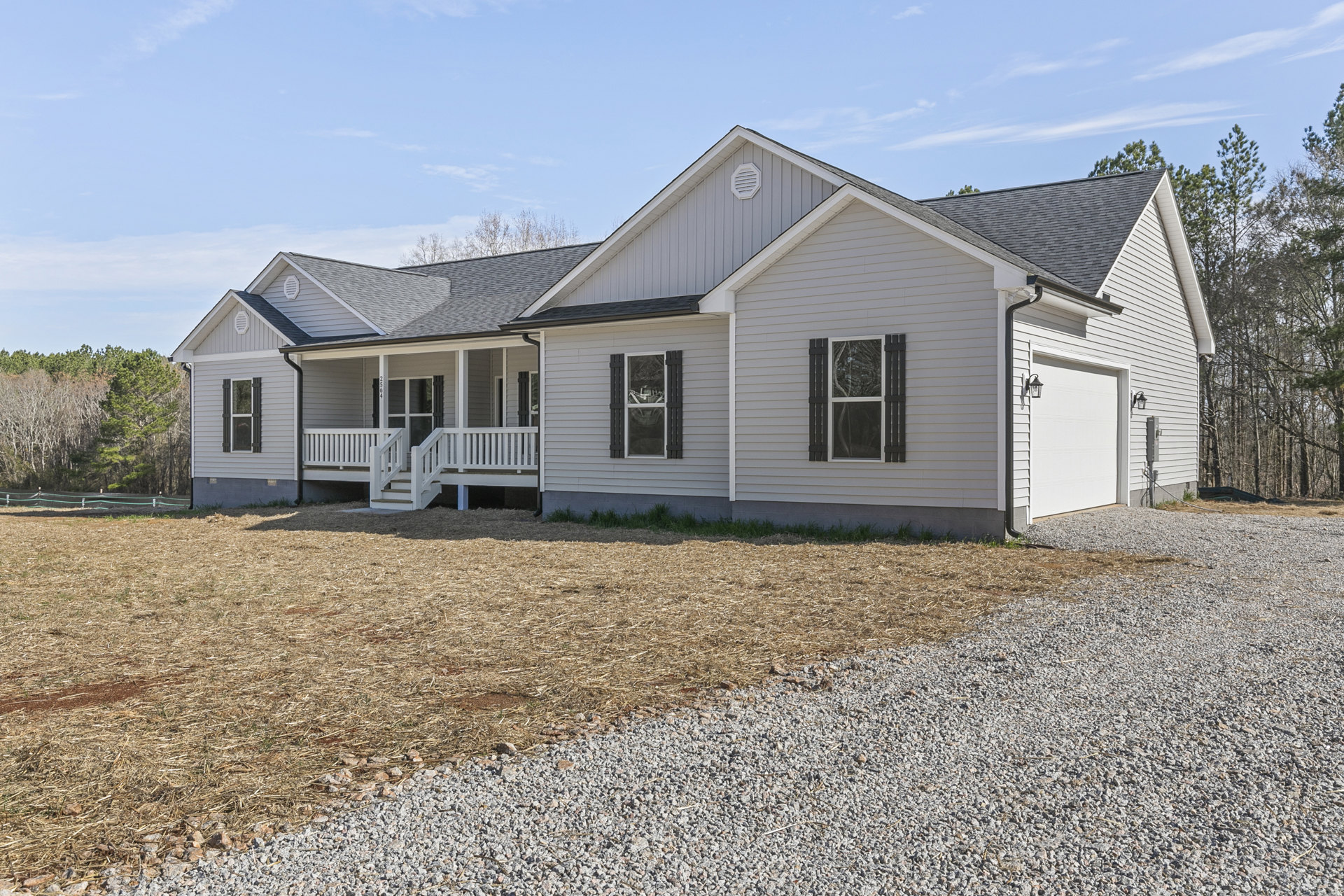 Two-story home with white siding, covered porch, gravel driveway bordered by grass, large windows including one with broken glass, white staircase visible near entrance, Robert