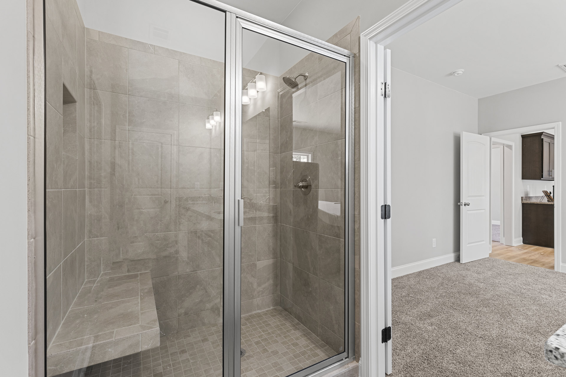 Walk-in shower with clear glass doors, white tile walls, chrome showerhead, and light-colored floor tiles