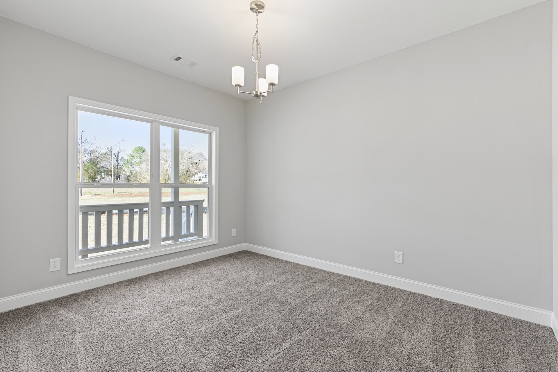 Bedroom with beige carpet, large window, white balcony railing, and view of deck surrounded by trees; plaster walls and ceiling molding visible.
