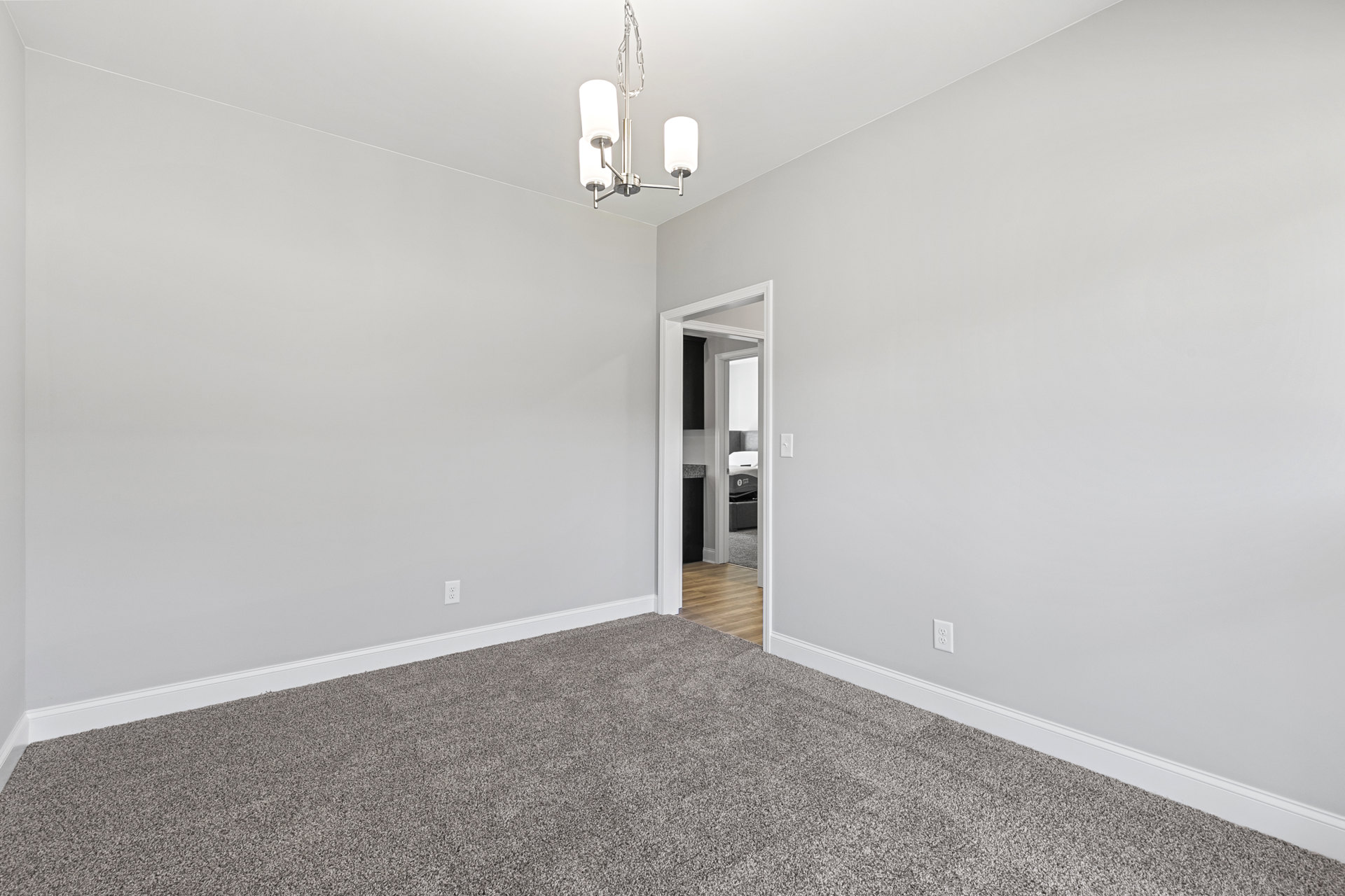Bedroom with light wood flooring, white plaster walls, open door, carpet, mattress, and modern chandelier.