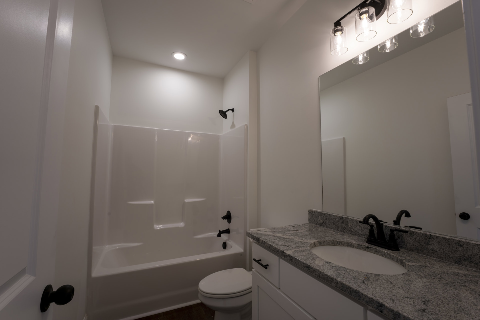 White tile bathroom with a rectangular sink, chrome faucet, white toilet, glass light fixture, and wall-mounted mirror
