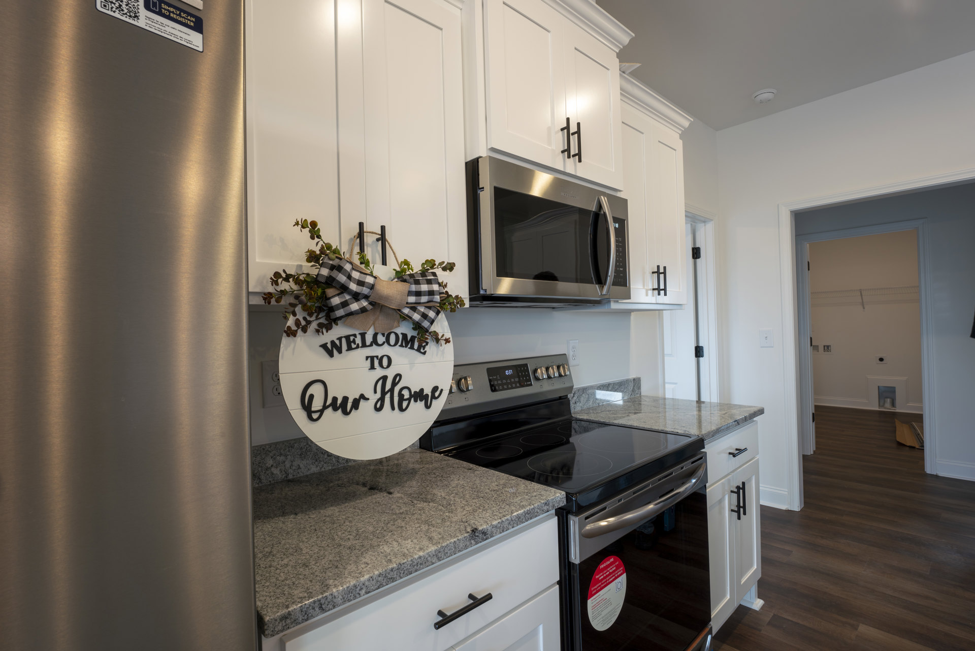 White cabinetry kitchen featuring a black stove, built-in microwave, light countertops, and decorative signs including one with a bow; round mirror mounted above counter.