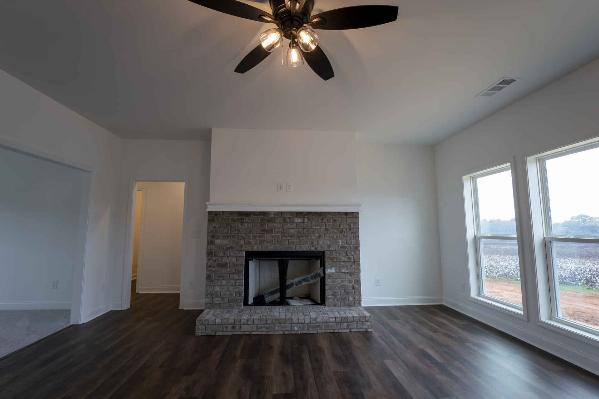 Ceiling fan with lights above a room featuring a brick fireplace with black metal frame, white walls with yellow trim, and a black metal tube wrapped in plastic.