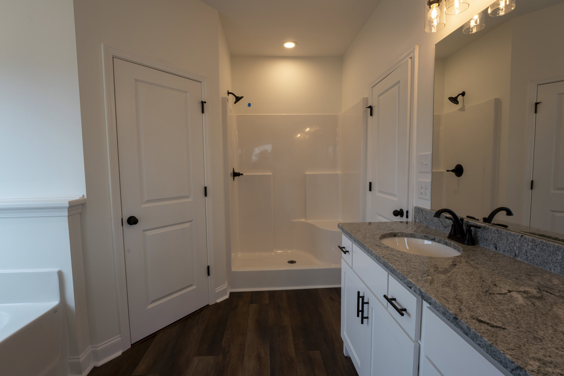 Modern bathroom featuring a white sink set in a black and white countertop, tiled shower with wall-mounted shower head, partial view of a bathtub, and contemporary lighting