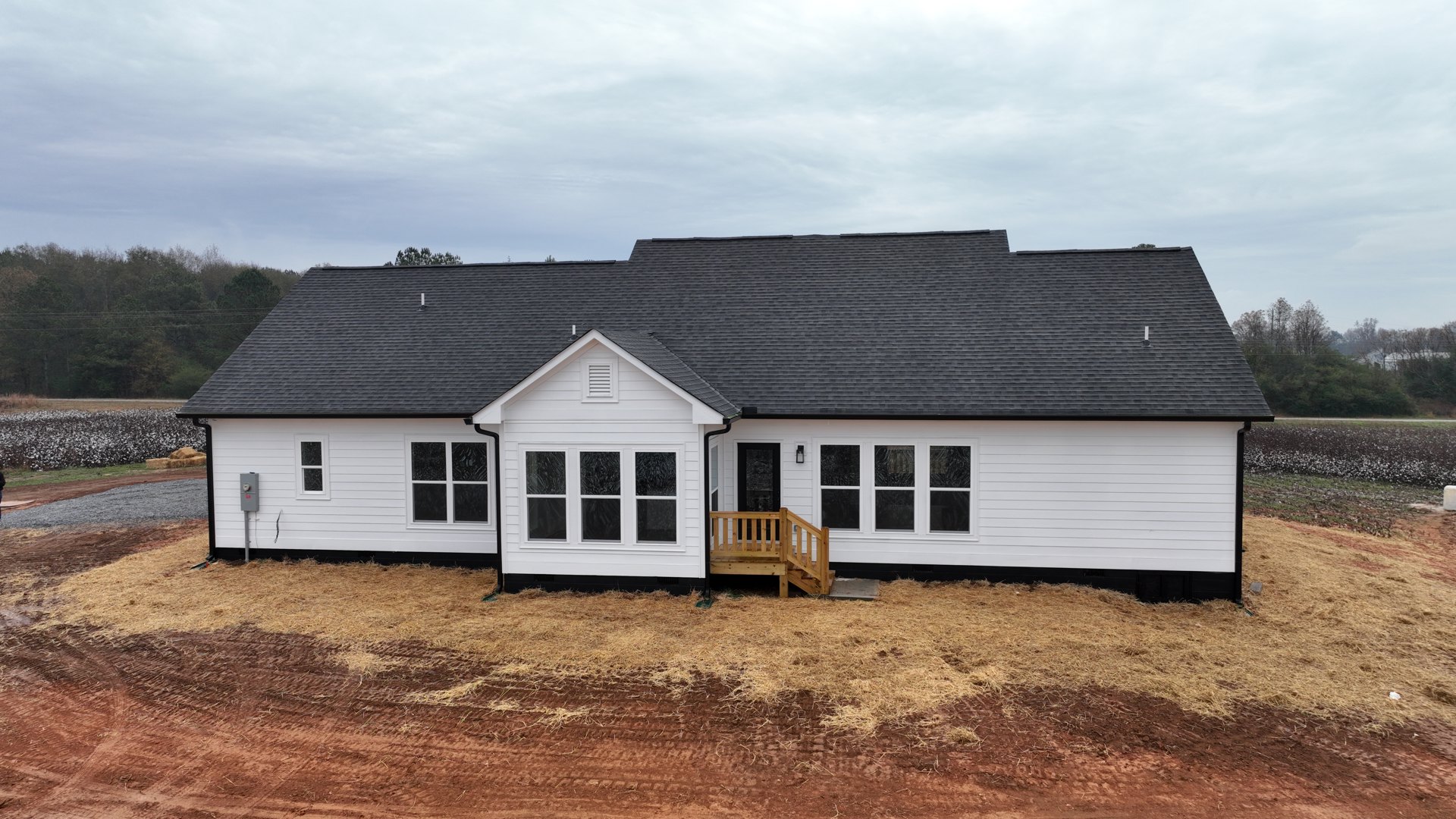 White house with black roof, wood deck and staircase, fenced yard with green grass, large windows featuring black and white trim.