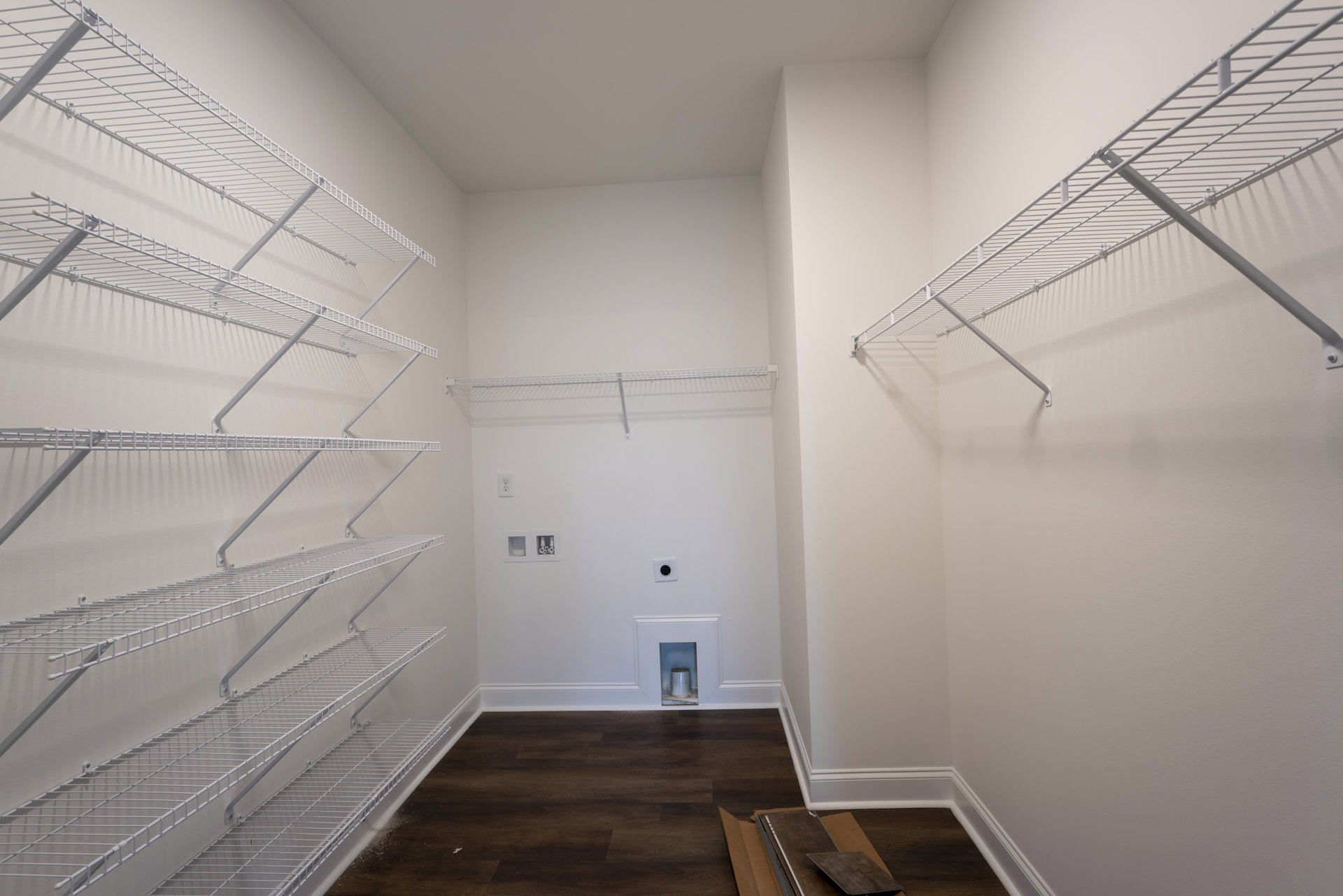 White built-in shelves with metal supports along a plaster wall, wood laminate flooring, and partial view of stairs in a modern interior room.