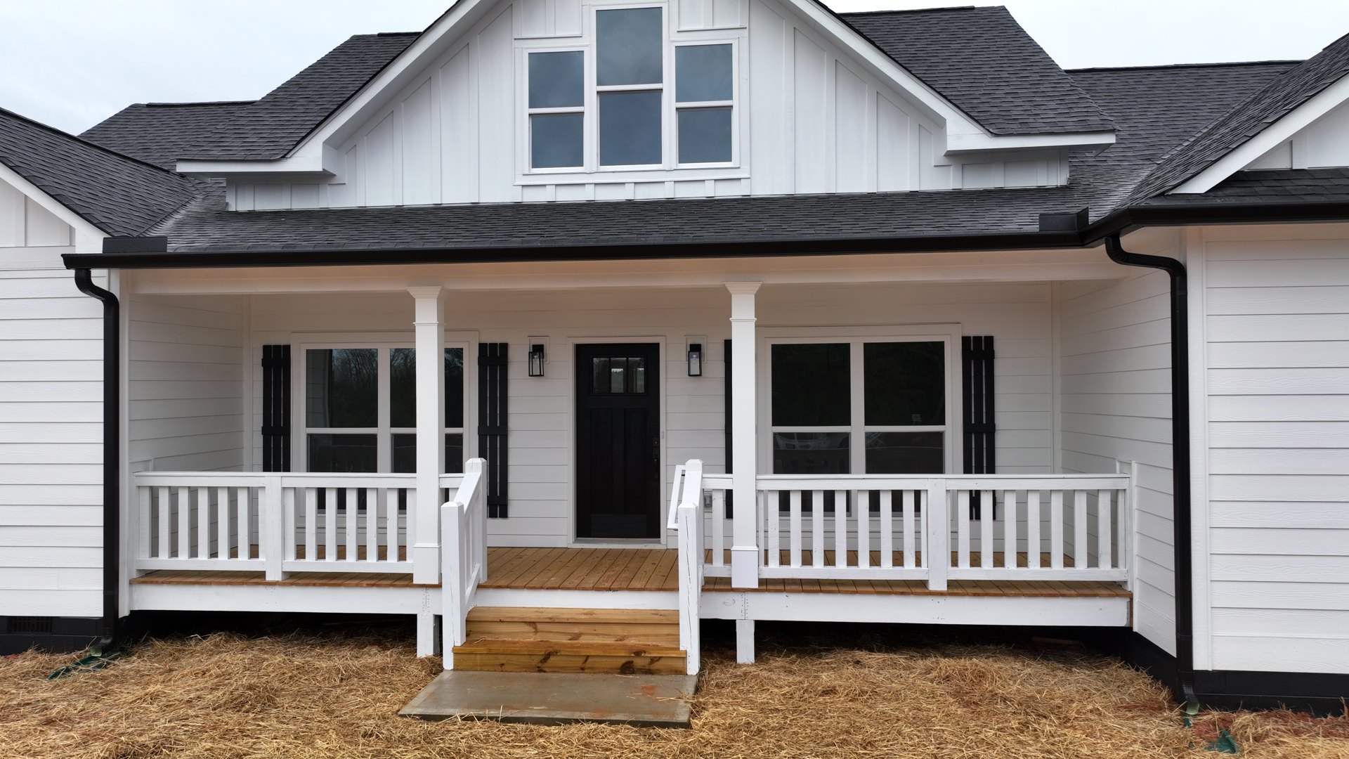 White siding house with covered front porch, black glass-paneled door, wooden railing, and multiple windows