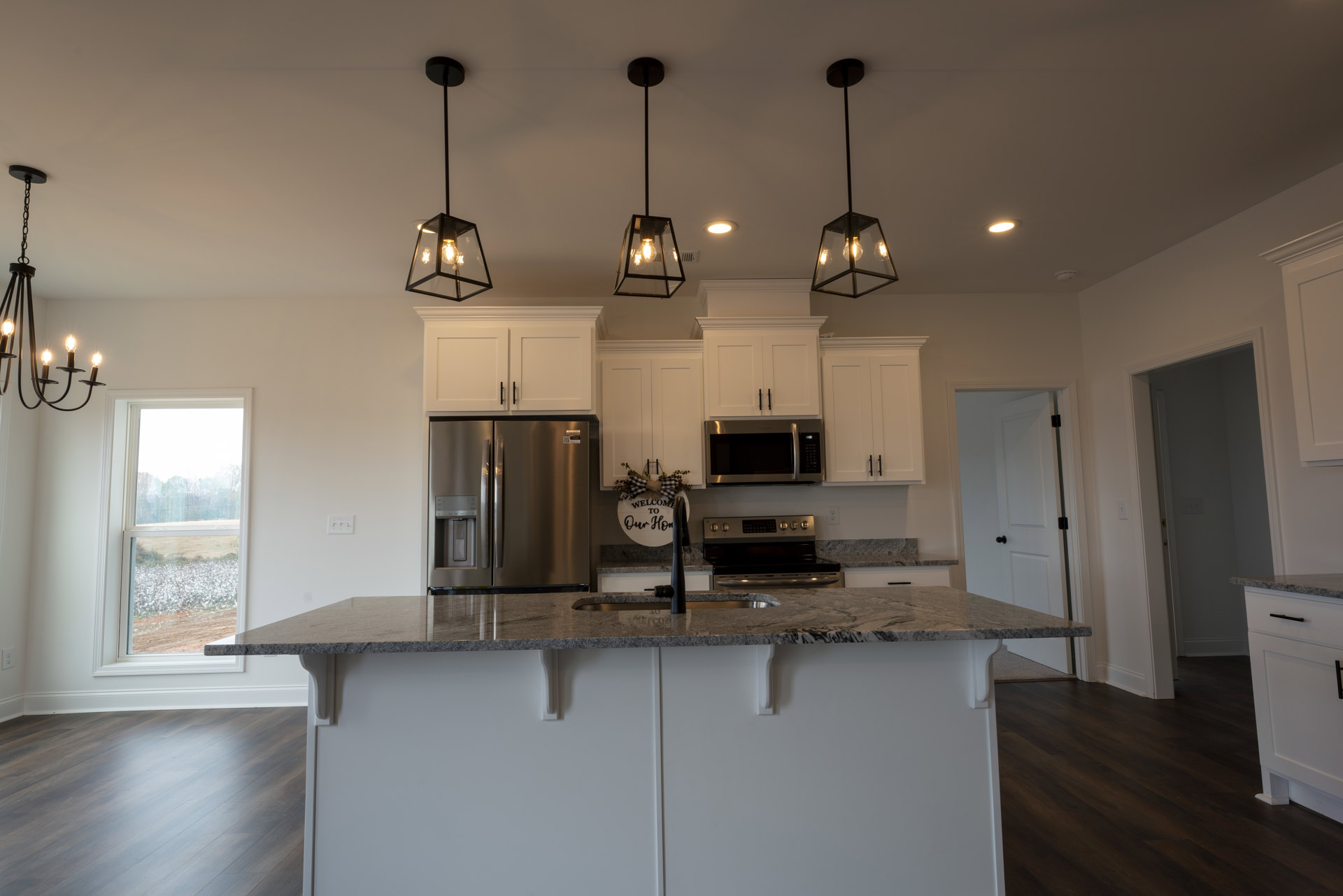 Modern kitchen featuring a central island with quartz countertop, stainless steel refrigerator with ice and water dispenser, open microwave oven, undermount sink, white cabinetry