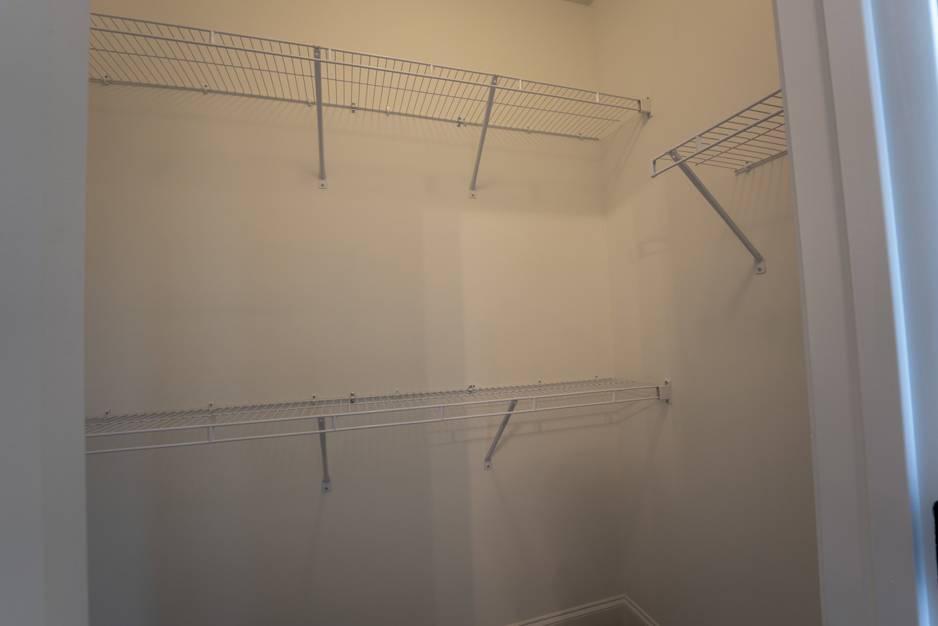 Corner closet with white metal shelves mounted on plaster walls, metal railing with vertical rods, and parallel shelving lines.