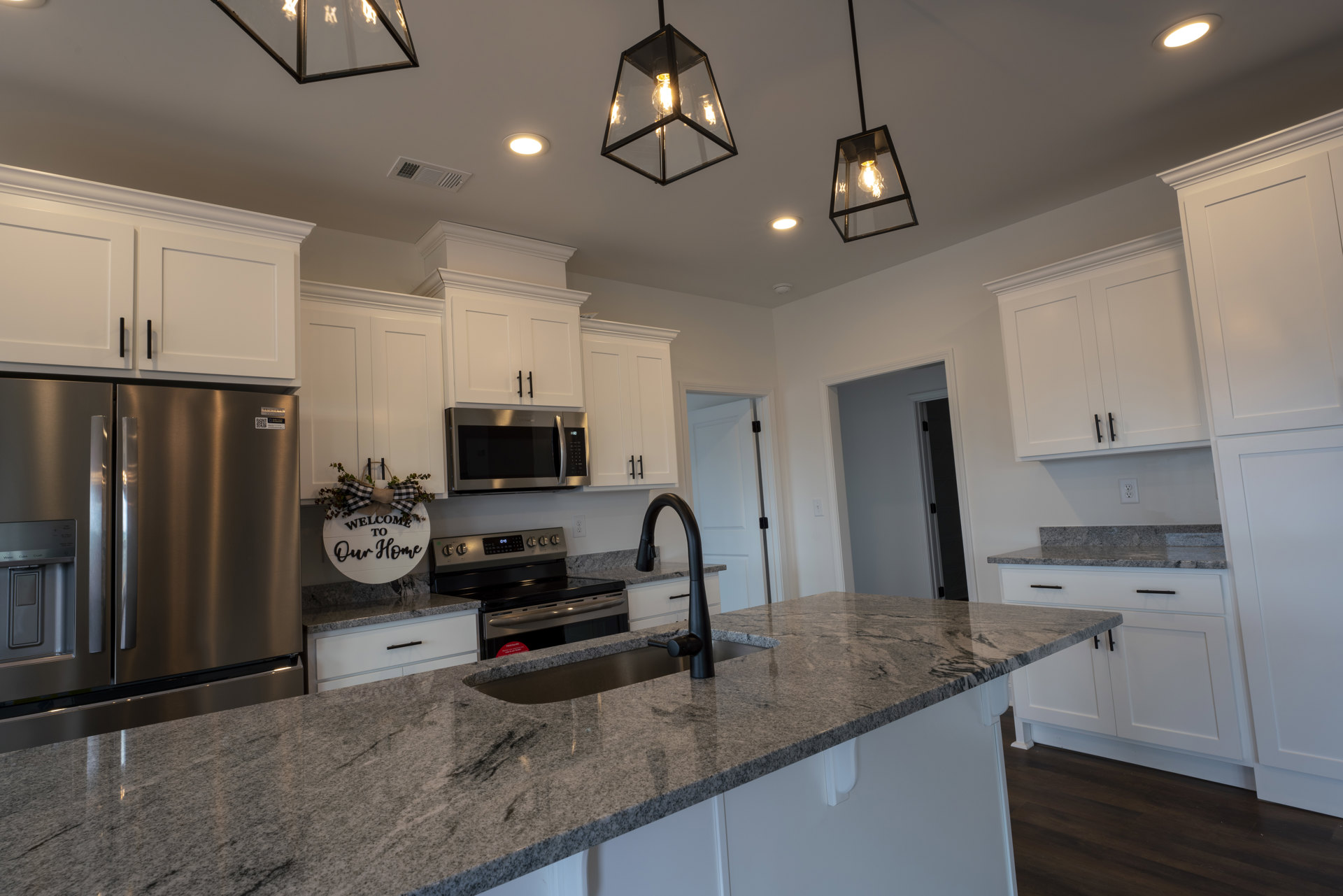 Modern kitchen with stainless steel appliances, undermount sink set in quartz countertop, white cabinetry, glass pendant light, and black-framed ceiling light fixture