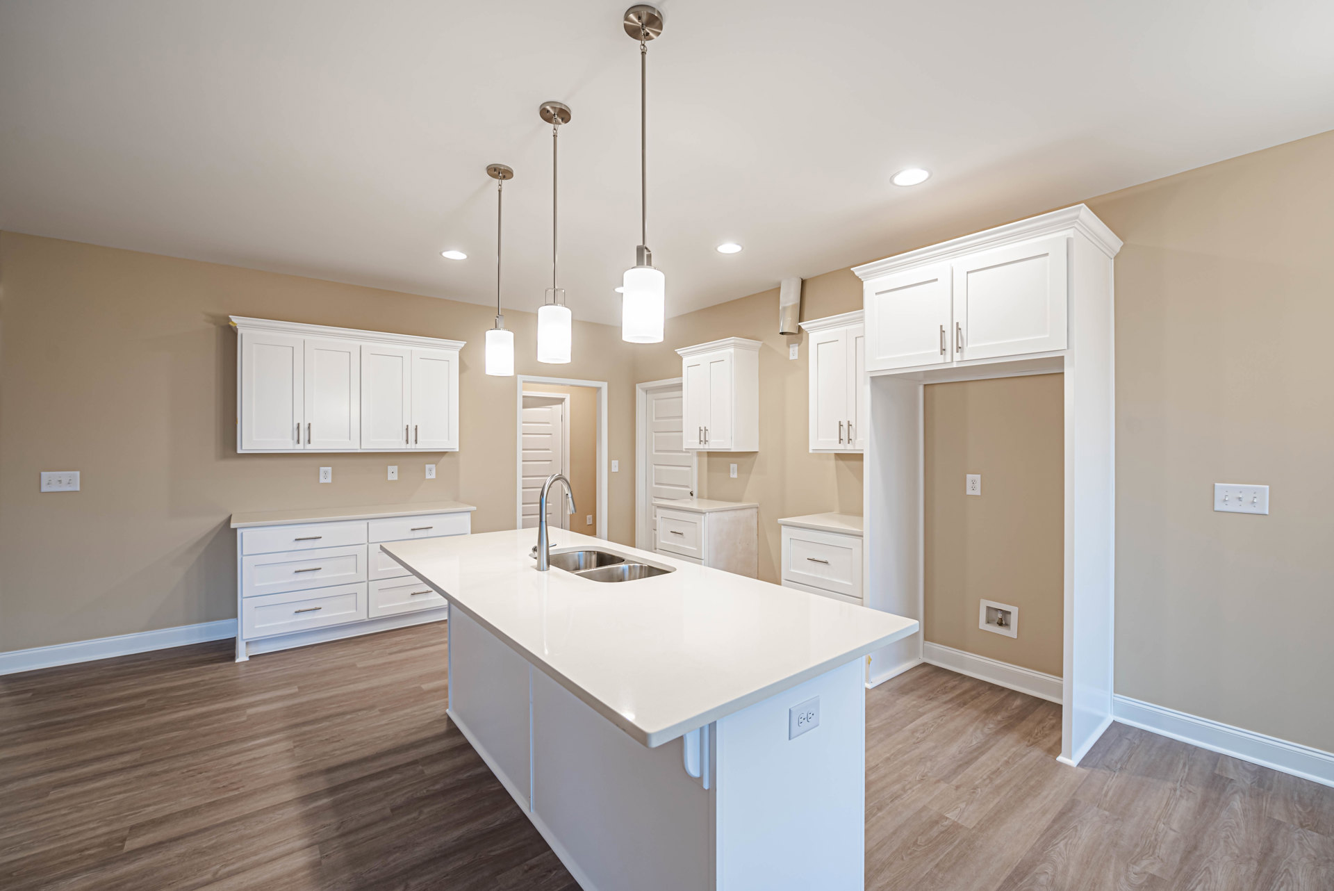 White kitchen with shaker cabinets, brushed metal handles, large white island featuring an undermount sink, quartz countertops, tile backsplash, and modern rectangular pendant