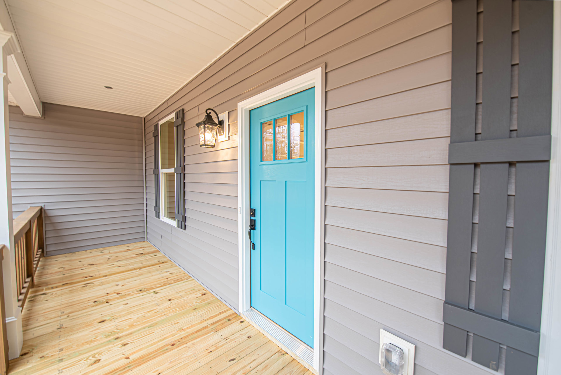 Blue front door with black handle, adjacent to white wall and wooden plank flooring, blue window with glass panes, close-up of light fixture and plastic box.