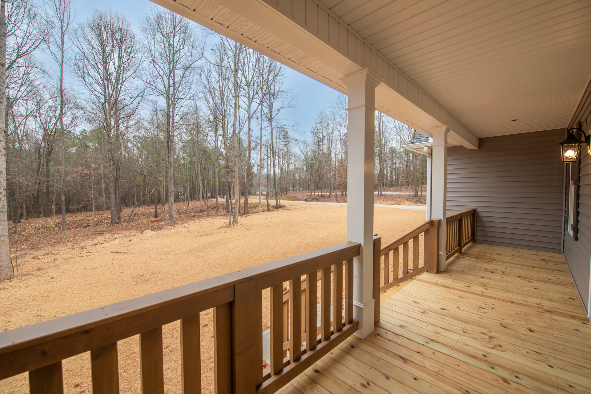 Wooden deck with railing overlooking grassy yard and dense trees, shaded by roof overhang