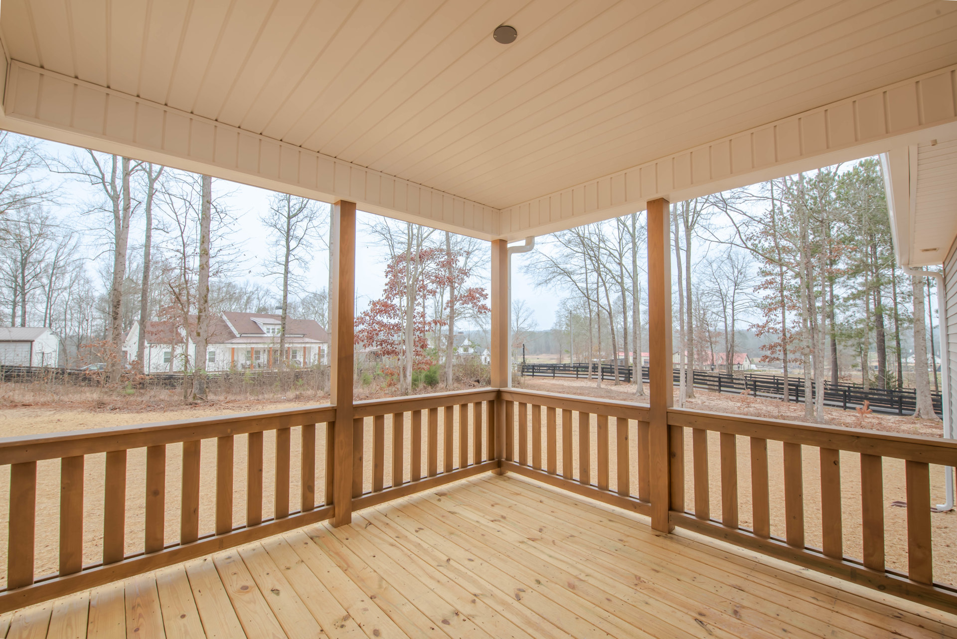 Wooden porch with railing, round ceiling light, overlooking trees, fence, and neighboring house