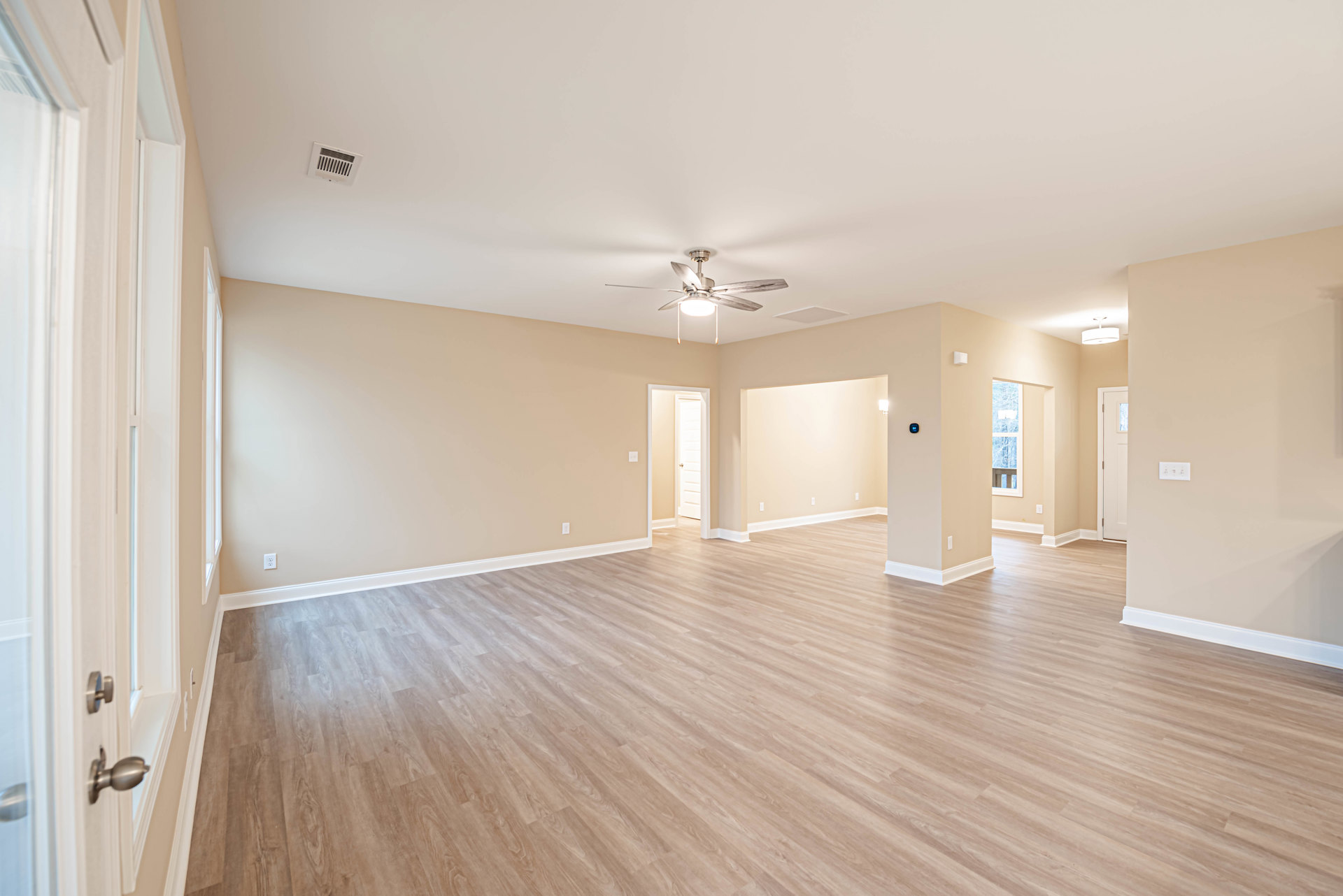 Spacious room with rich hardwood flooring, white walls, ceiling fan with light, ceiling vent, and visible light switch