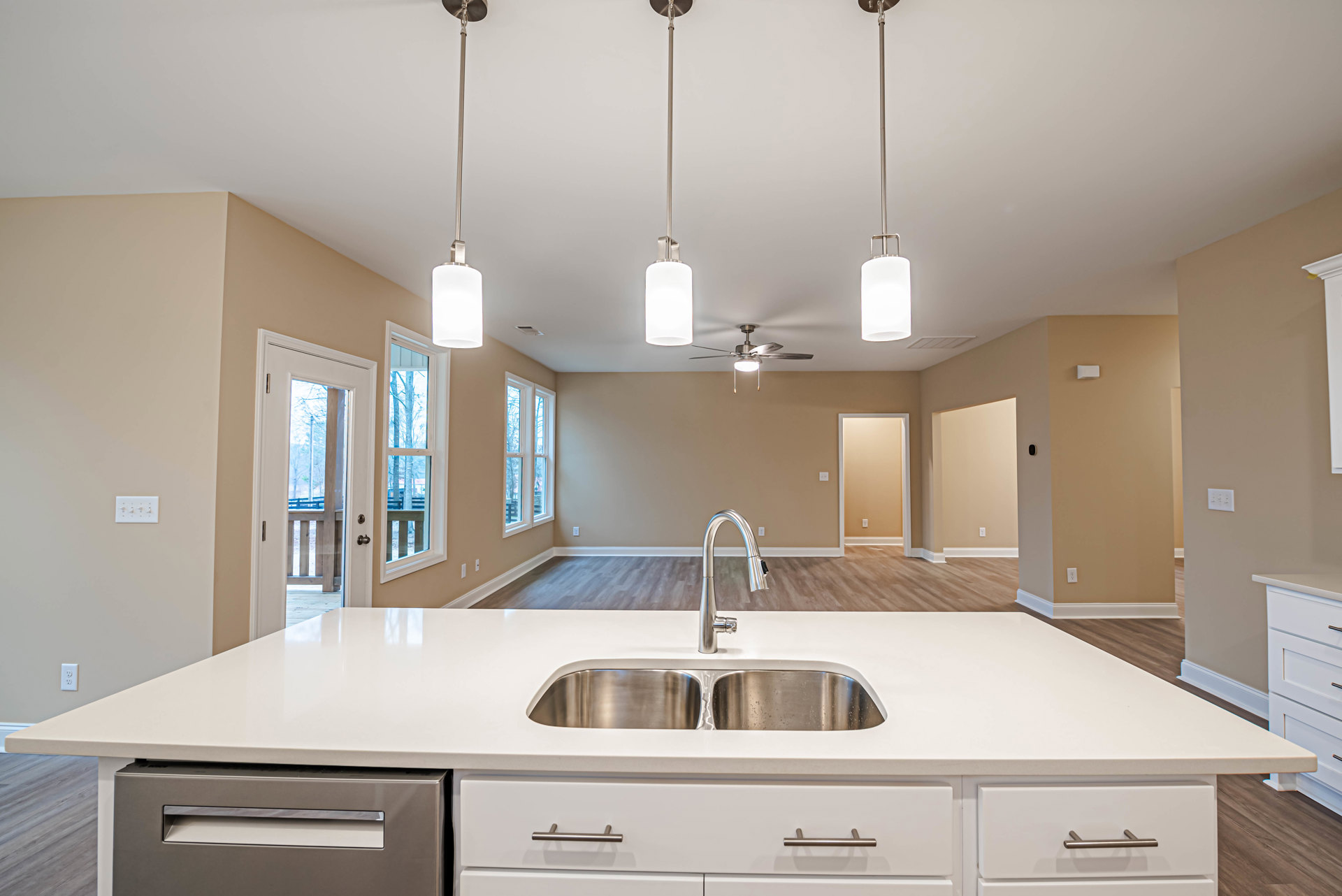 Modern kitchen with stainless steel sink and faucet set in a spacious open floor plan, featuring light cabinetry, stone countertops, and integrated drawers