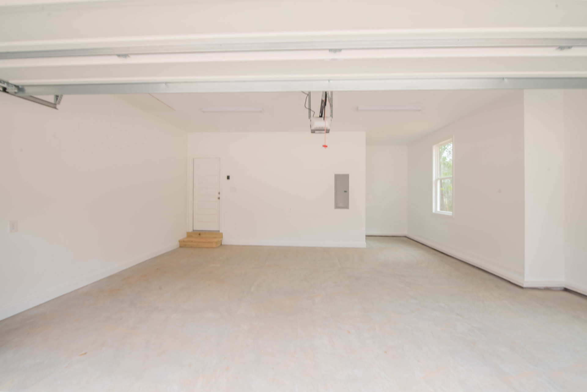 White-walled room with white flooring, white door featuring silver knobs and a sign, large window, white ceiling with exposed metal rods, and close-up of wood surface.