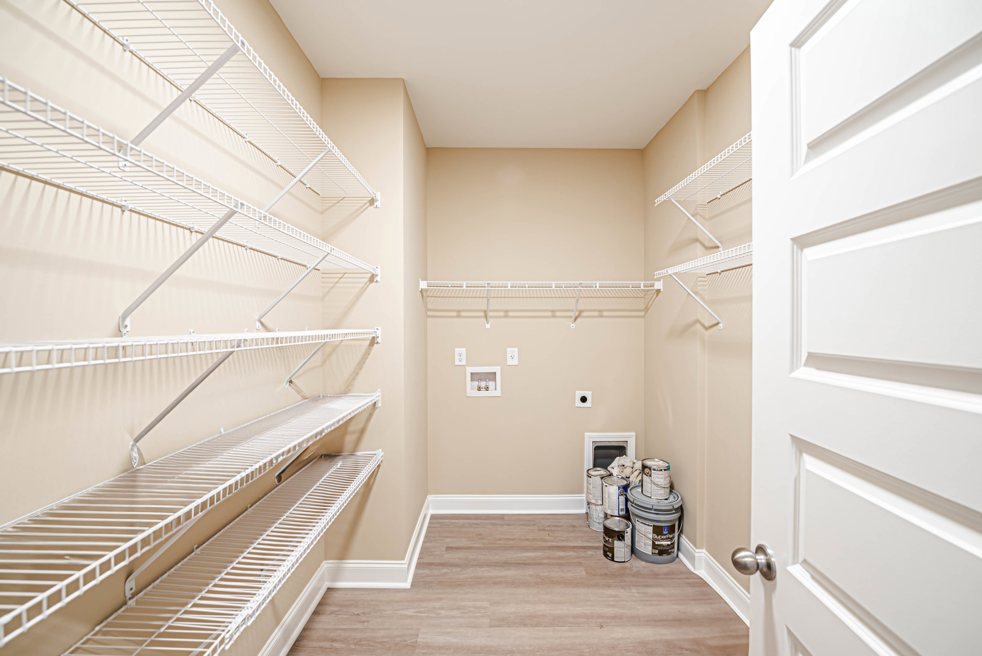 Empty walk-in closet with white built-in shelves, white metal rods, and a white door with brushed metal knob