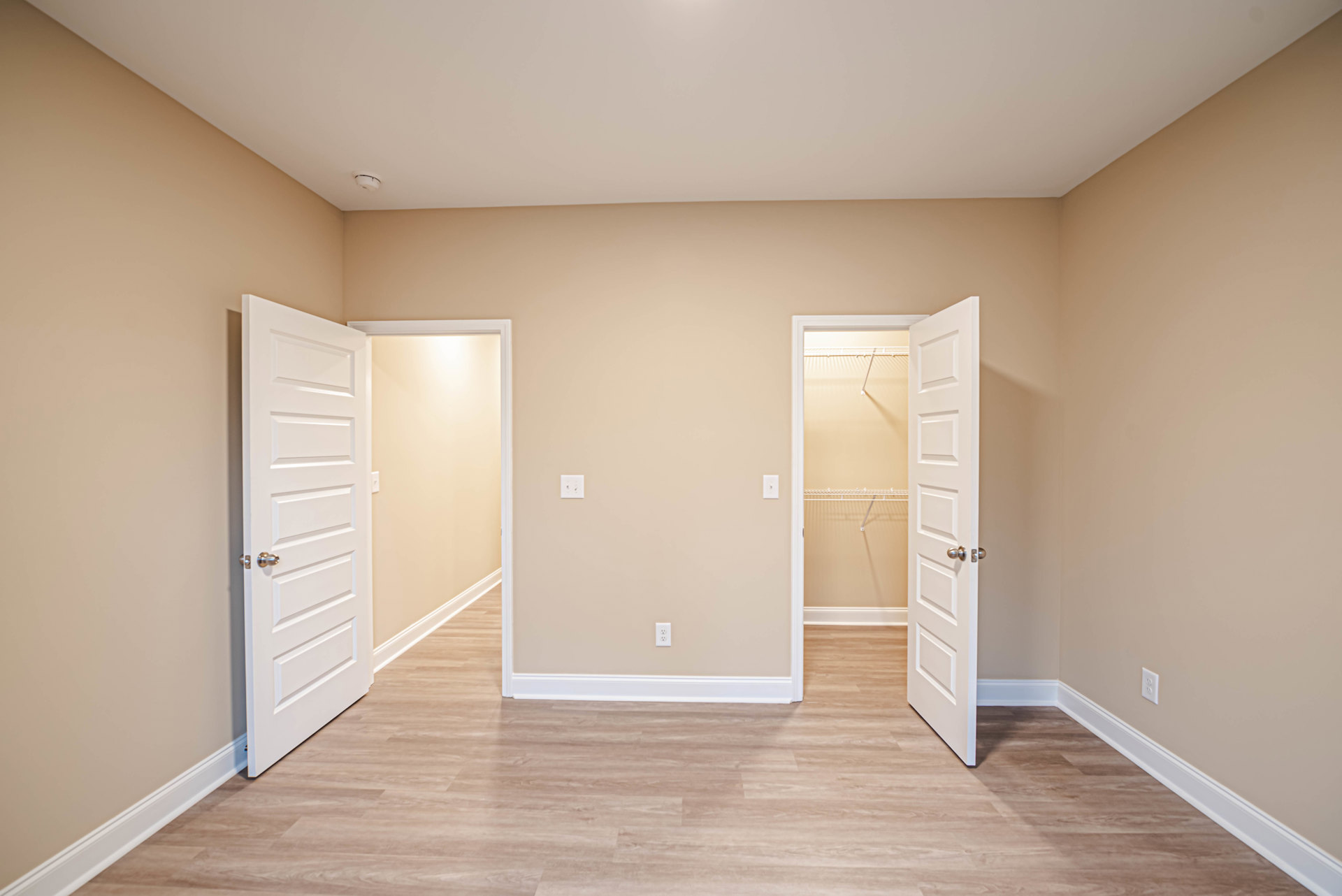 Room with wood flooring, white baseboards, two open white doors with silver hardware, and a closet featuring a white shelf