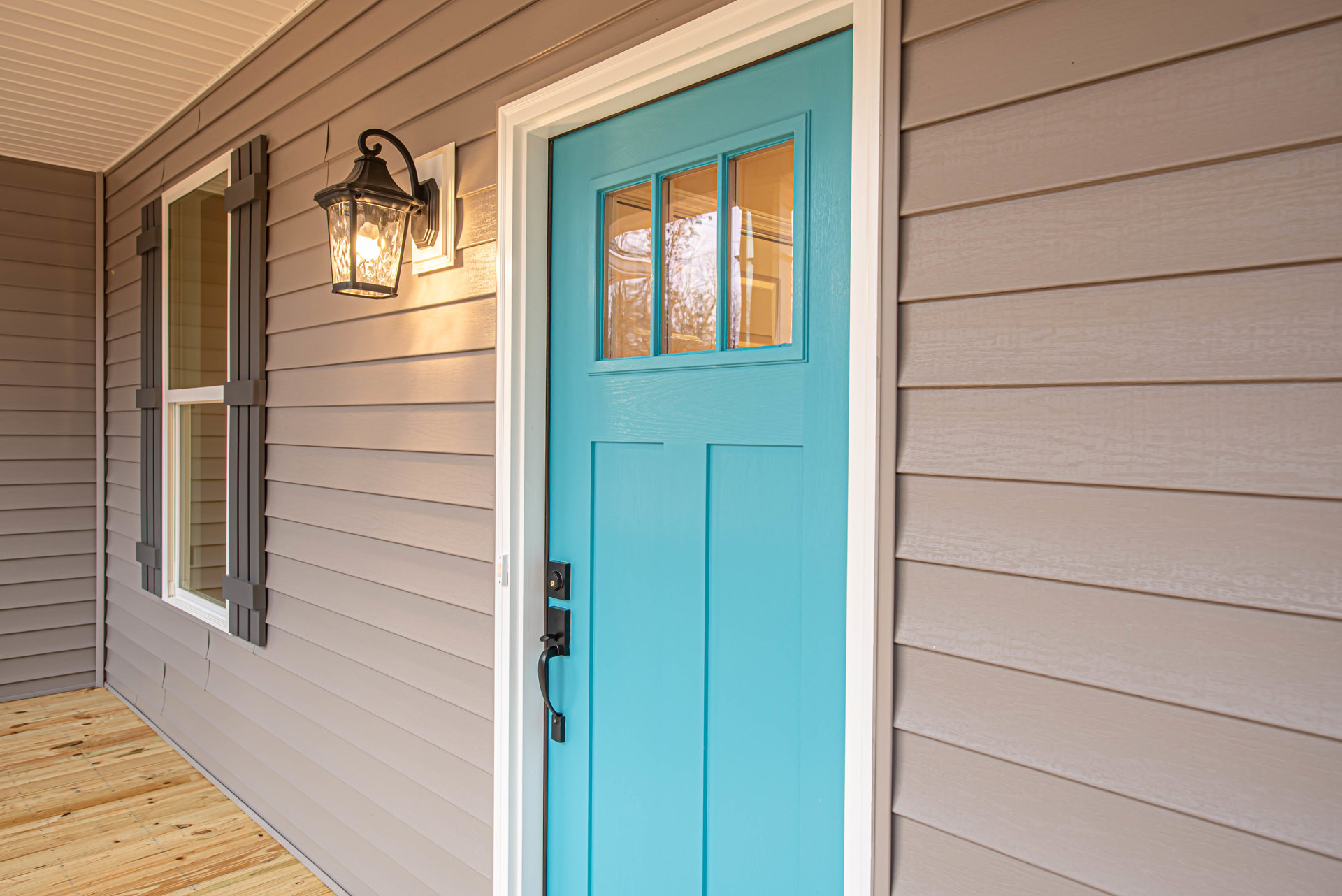 Blue front door with black handle, adjacent window with matching blue frame, wood flooring, wall-mounted light fixture, white exterior wall