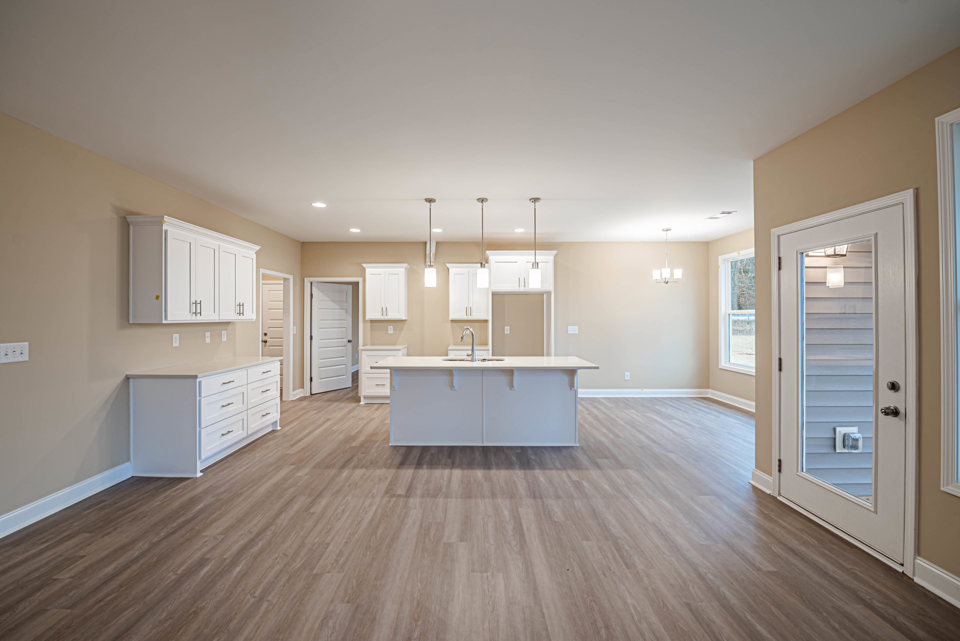 Open kitchen and dining area featuring wood flooring, white cabinetry, a white kitchen island with drawers, sleek countertop with built-in faucet, and adjacent door with light