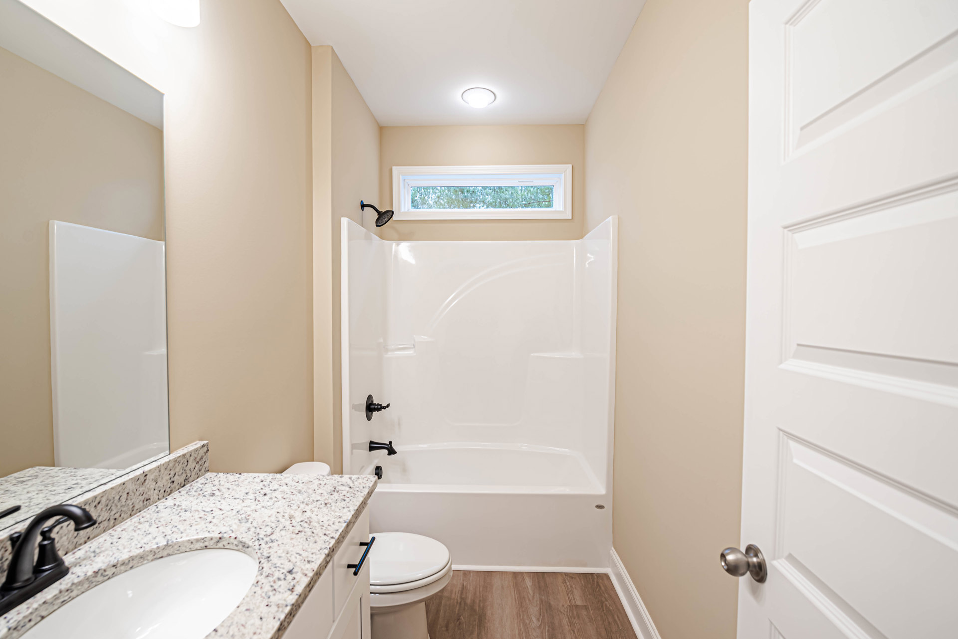 Bathroom with white tile walls, white bathtub featuring black faucets, white sink and toilet, rectangular wall-mounted mirror, and window with white frame.