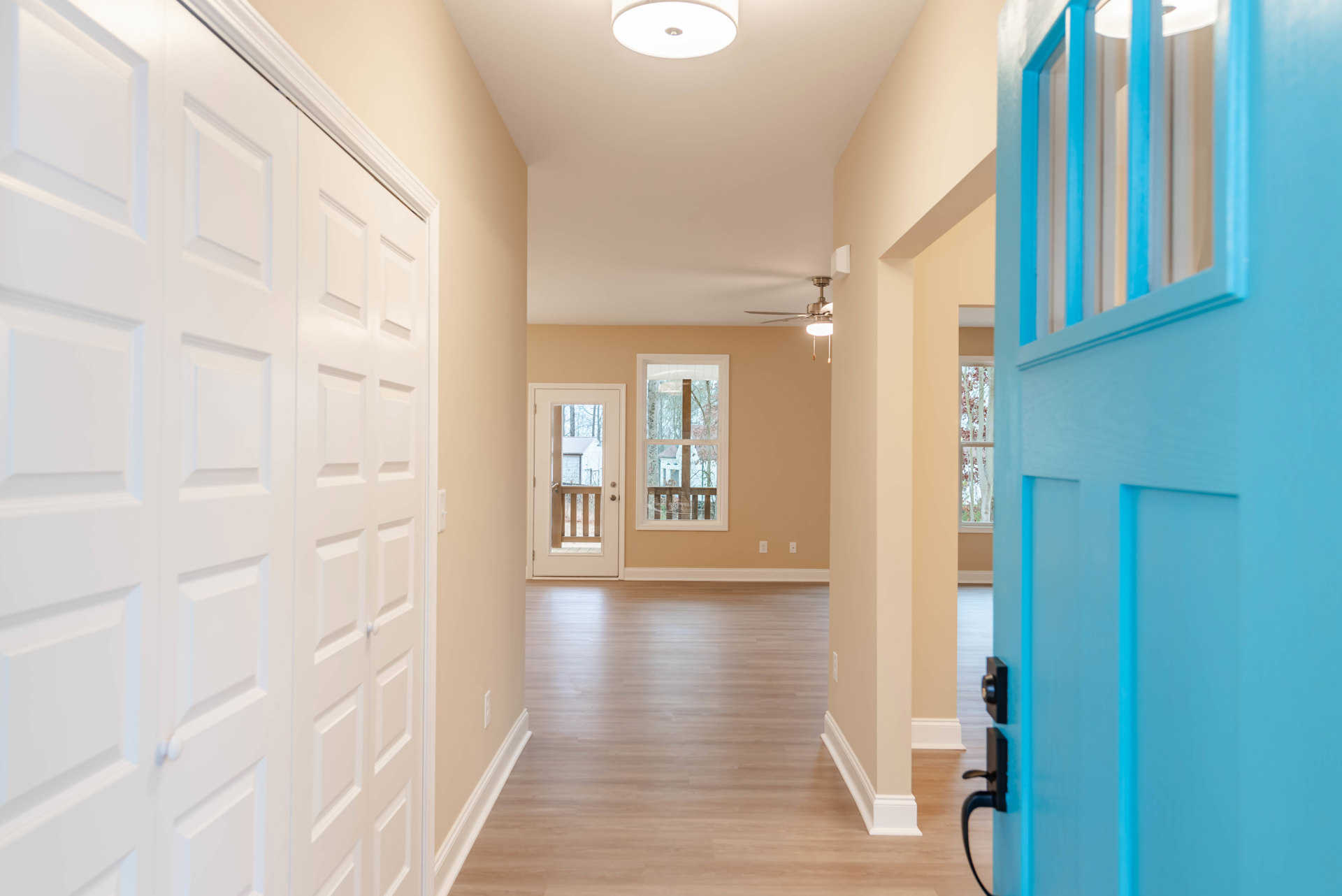 Hallway with hardwood flooring, blue door, white walls, window with wooden frame, white paneled door, and ceiling light fixture