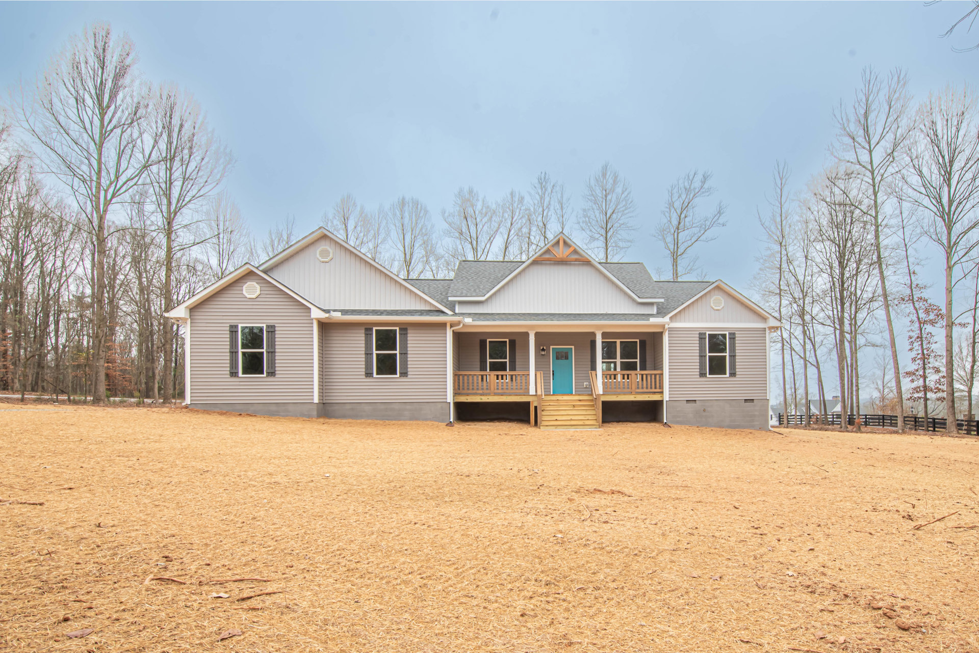 Two-story house with blue front door, white-framed windows, attached garage, covered porch, and expansive grassy yard bordered by mature trees.