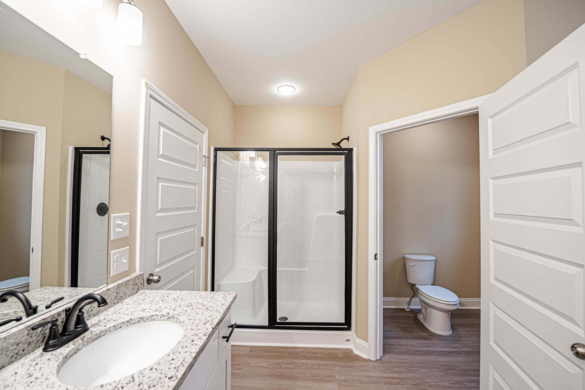 Modern bathroom featuring a glass-enclosed shower, white ceramic sink with chrome faucet, wall-mounted mirror, and tiled walls; toilet with tank visible beside the sink, white door