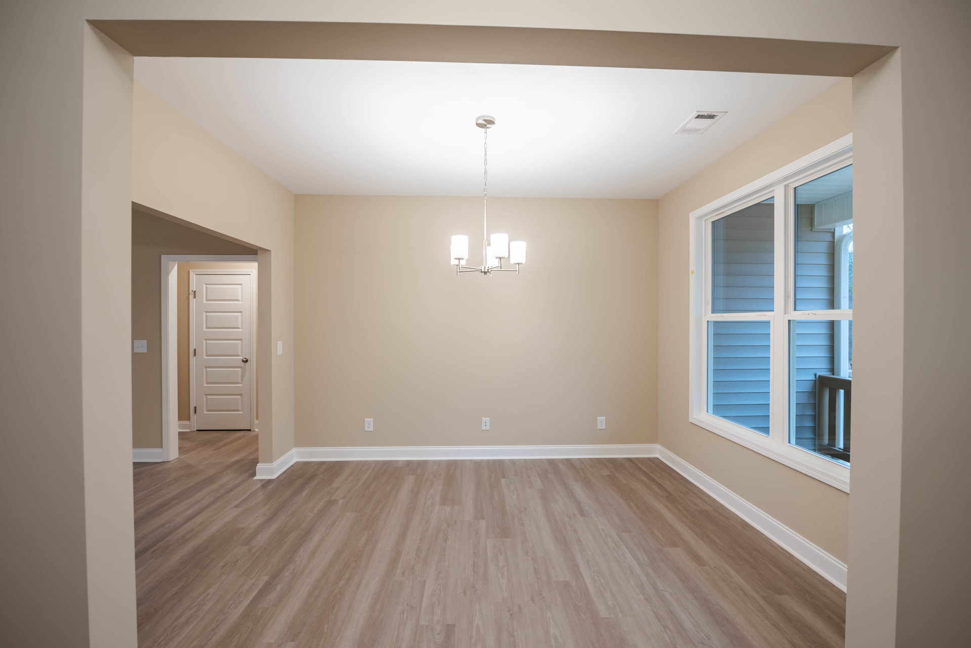 Wood flooring with white baseboard trim, white door with silver handle, ceiling-mounted light fixture, window with white frame, neutral walls