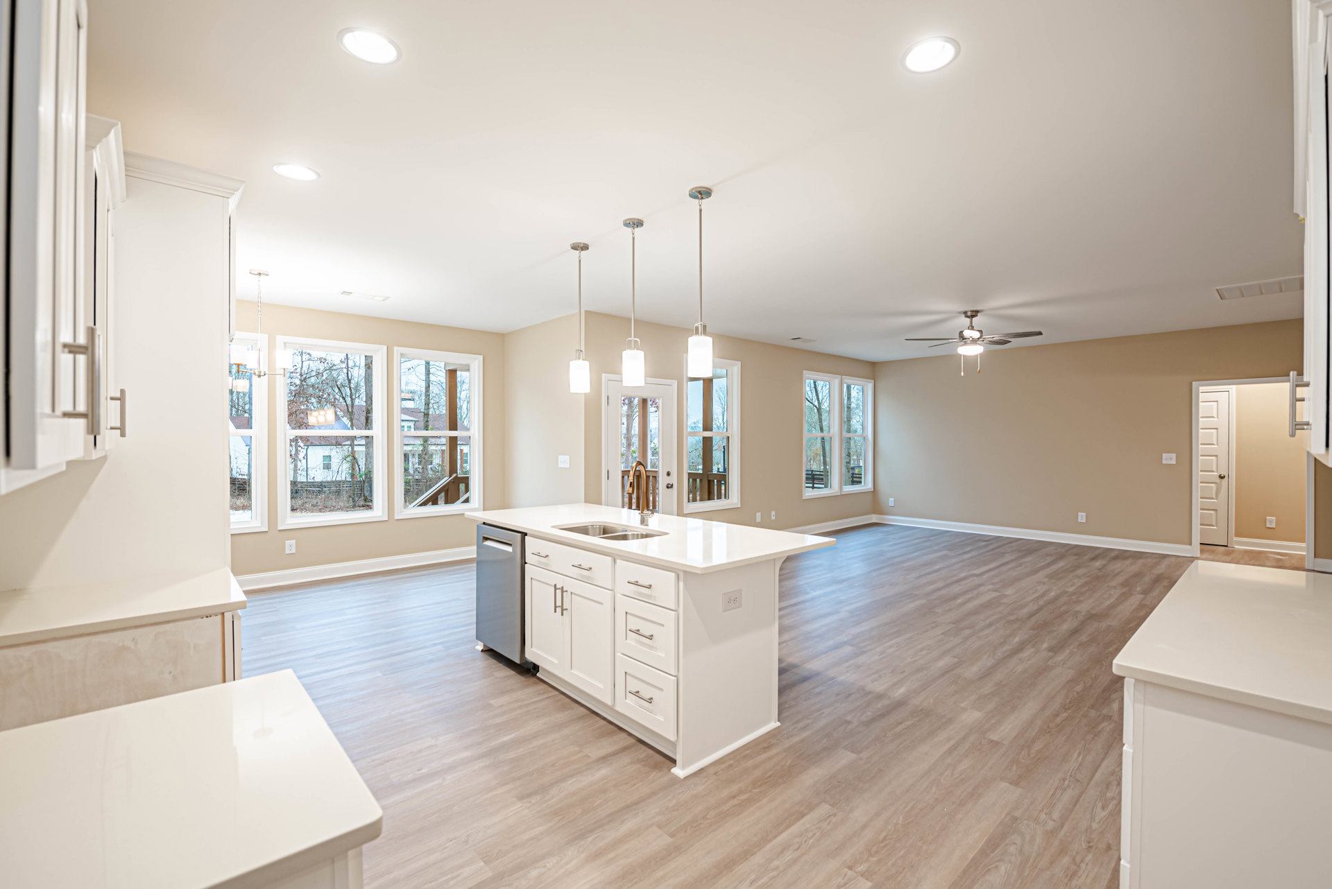 Open kitchen and living room with wood flooring, central island featuring sink and dishwasher, white rectangular appliance with black trim, ceiling light fixture, white dining
