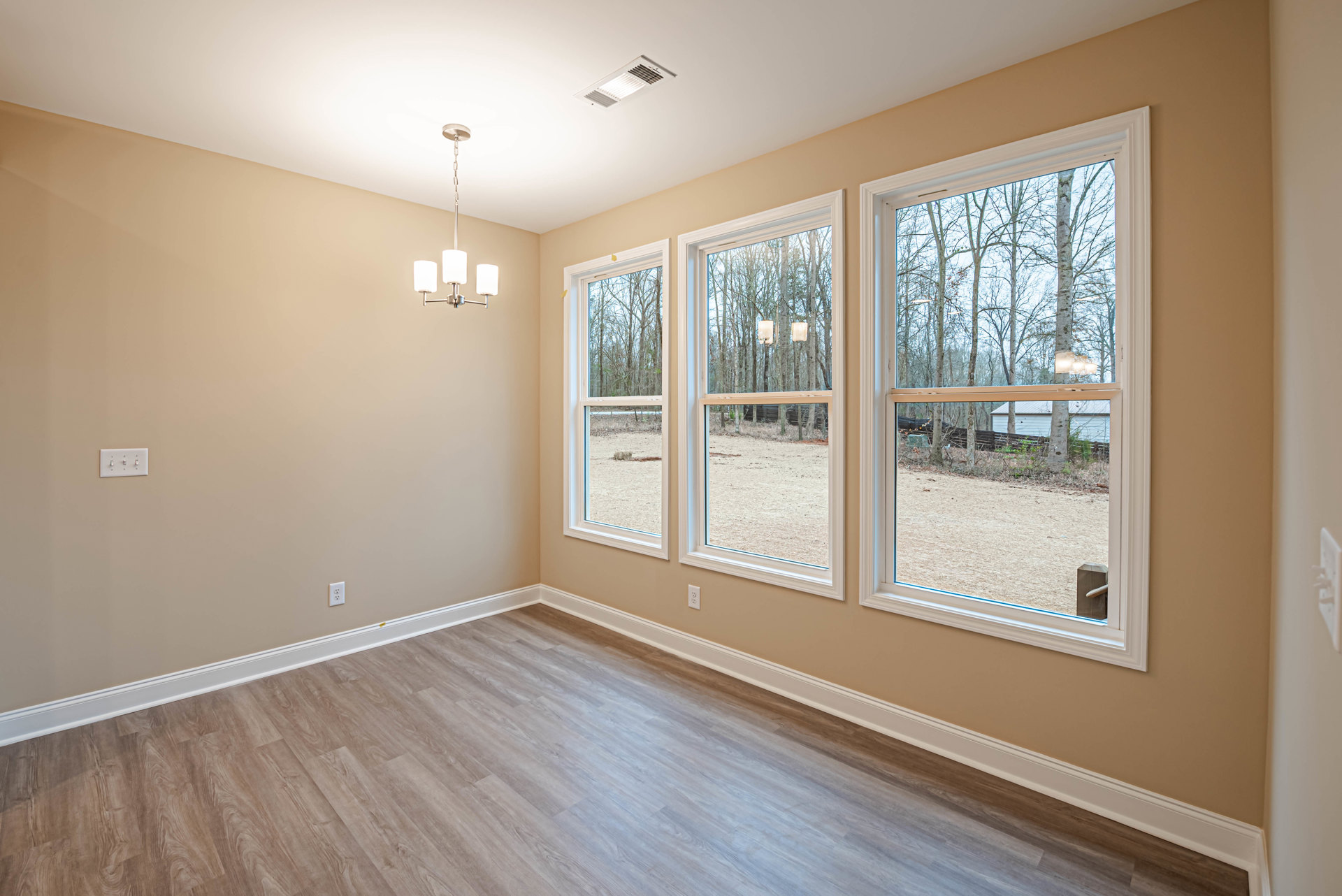 Hardwood floor with white walls, electrical outlet, ceiling vent, and a row of windows overlooking trees