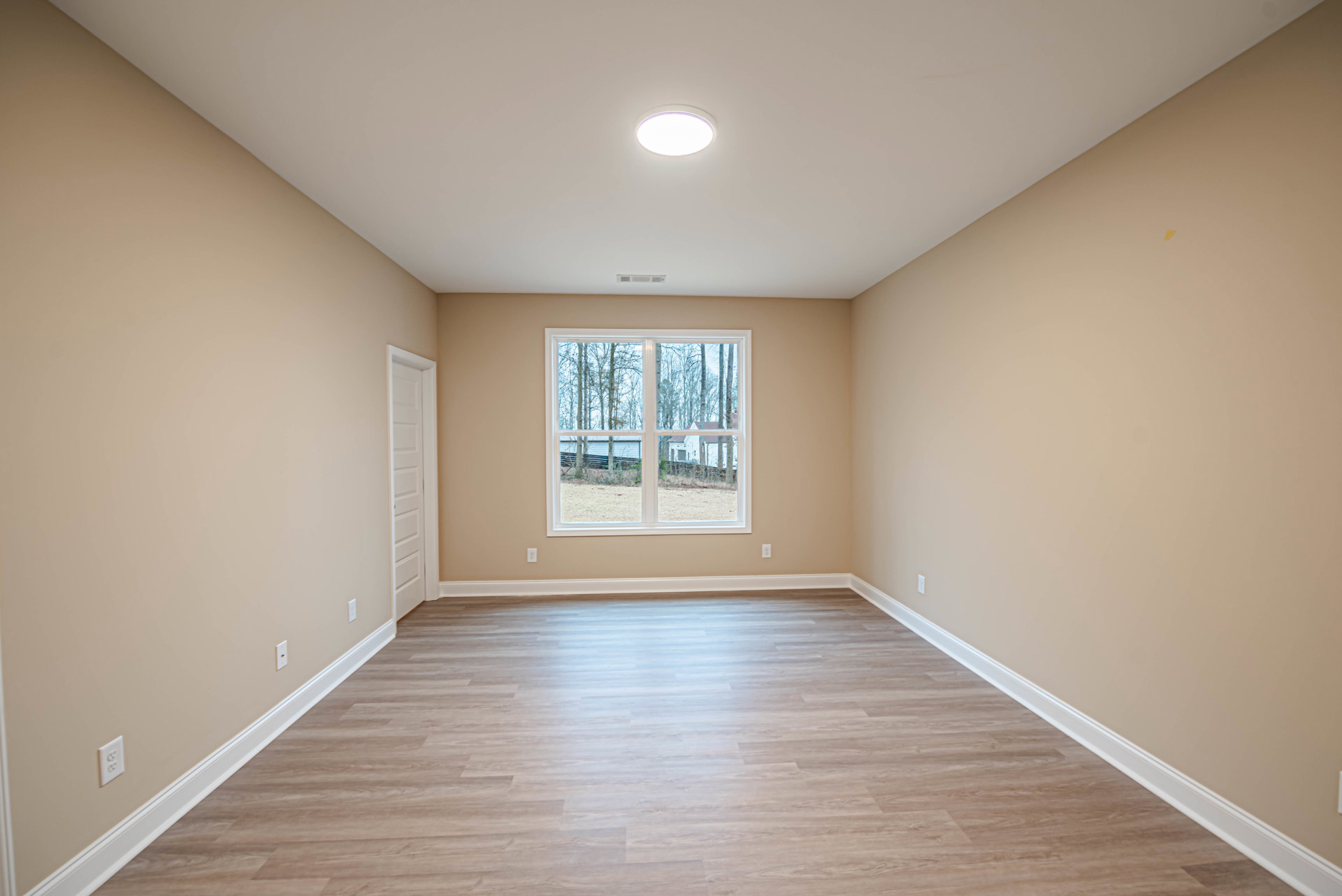 Sunlit room featuring a large window with views of trees, hardwood flooring with white baseboard trim, smooth plaster walls, recessed ceiling light, and a white door partially