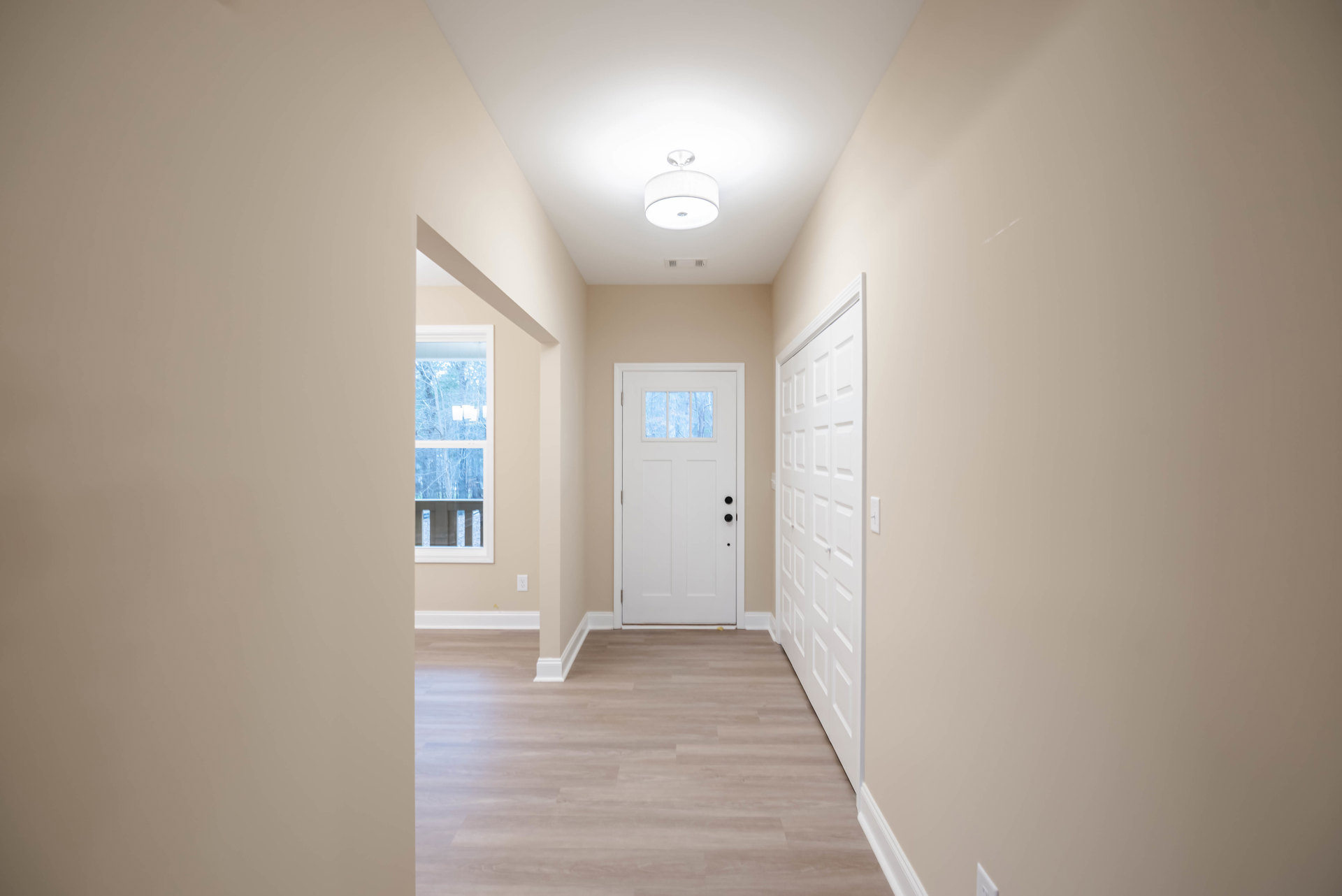 Hallway with wood flooring, white trim, and a white door featuring a frosted window; white light fixture with shade mounted on the ceiling