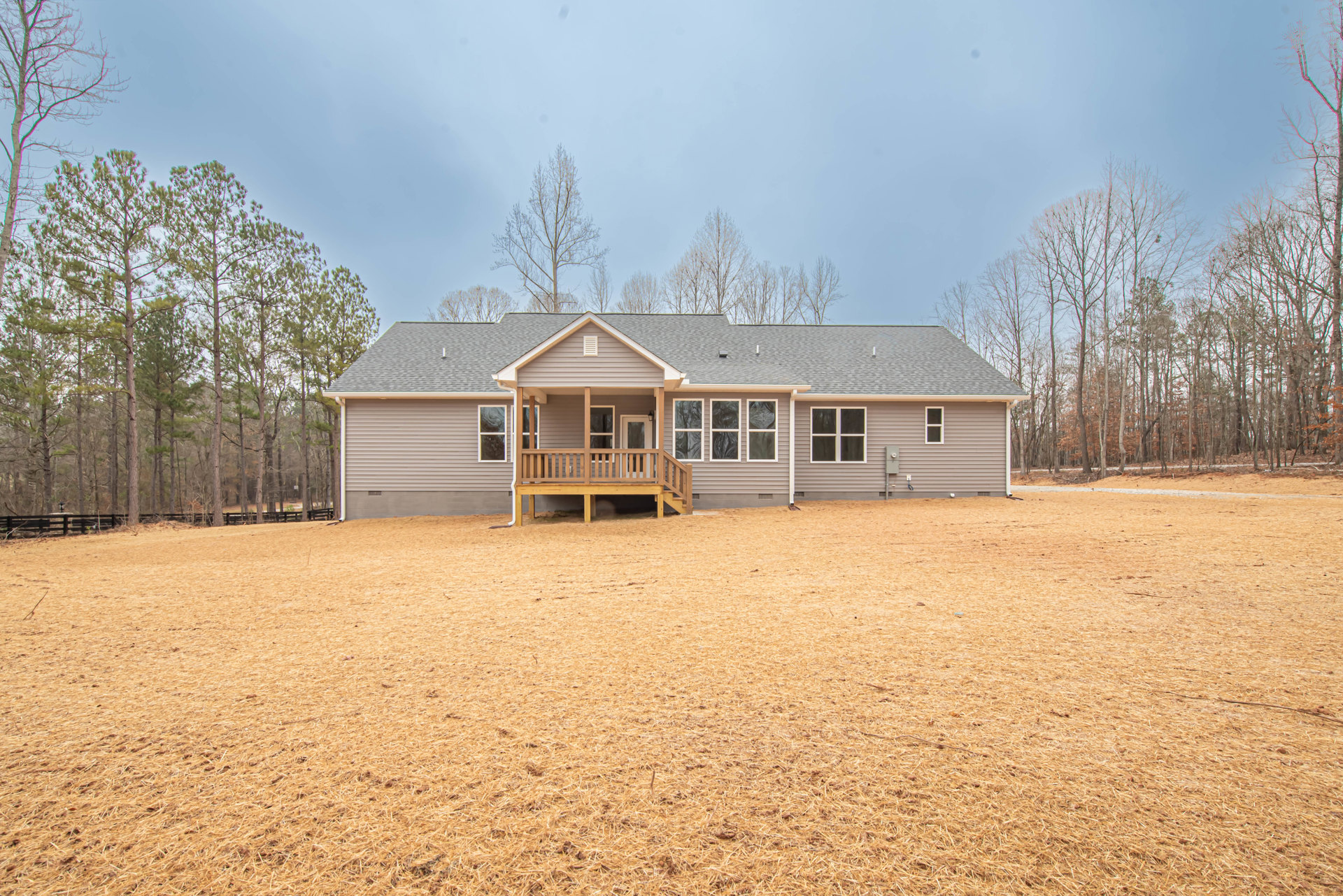 Two-story house with white siding, wooden deck with railing, large grassy yard, mature trees, and multiple windows and doors