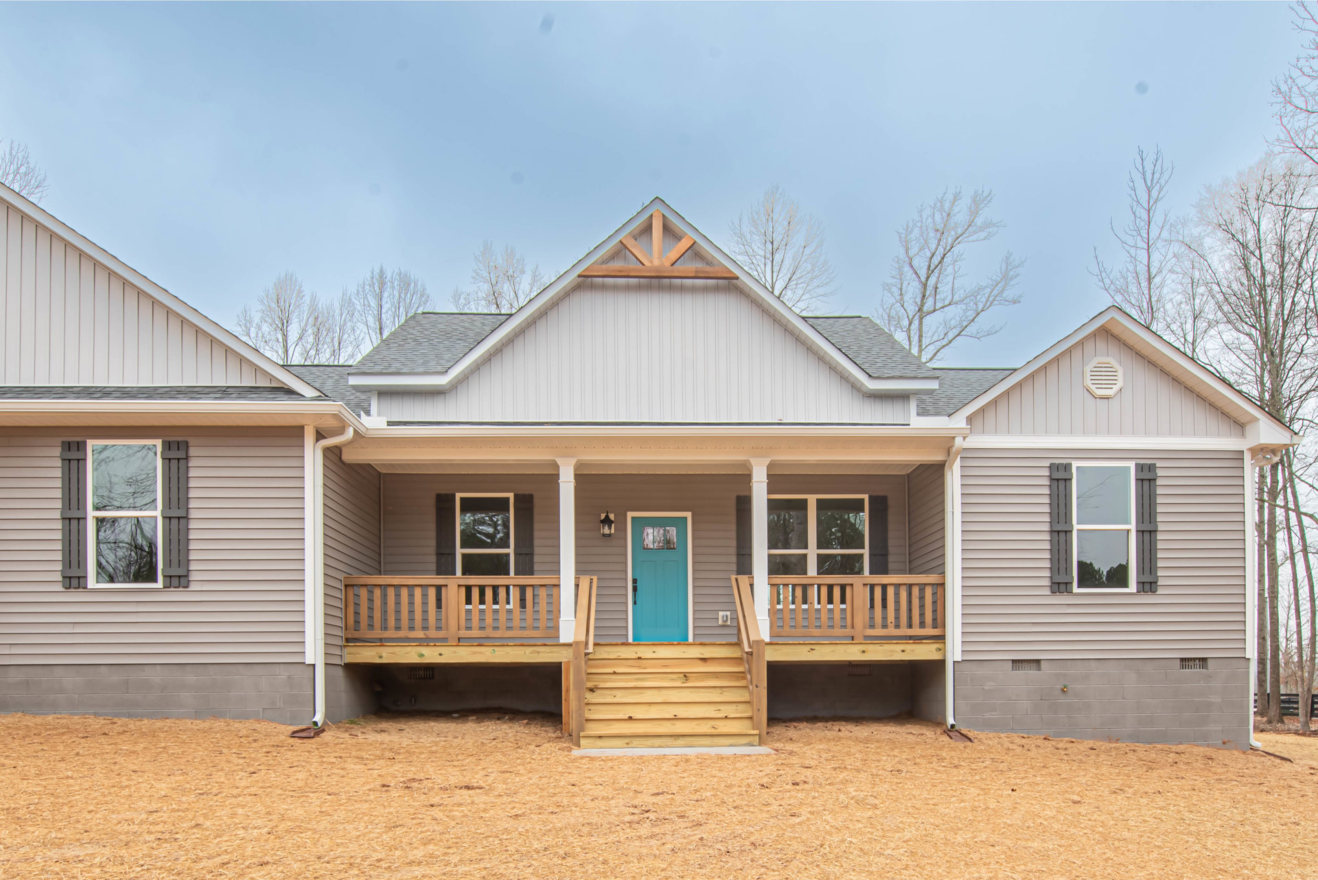 Blue front door with glass window, covered porch, white siding and vent, wood shavings scattered on ground, windows reflecting trees, one window with broken glass