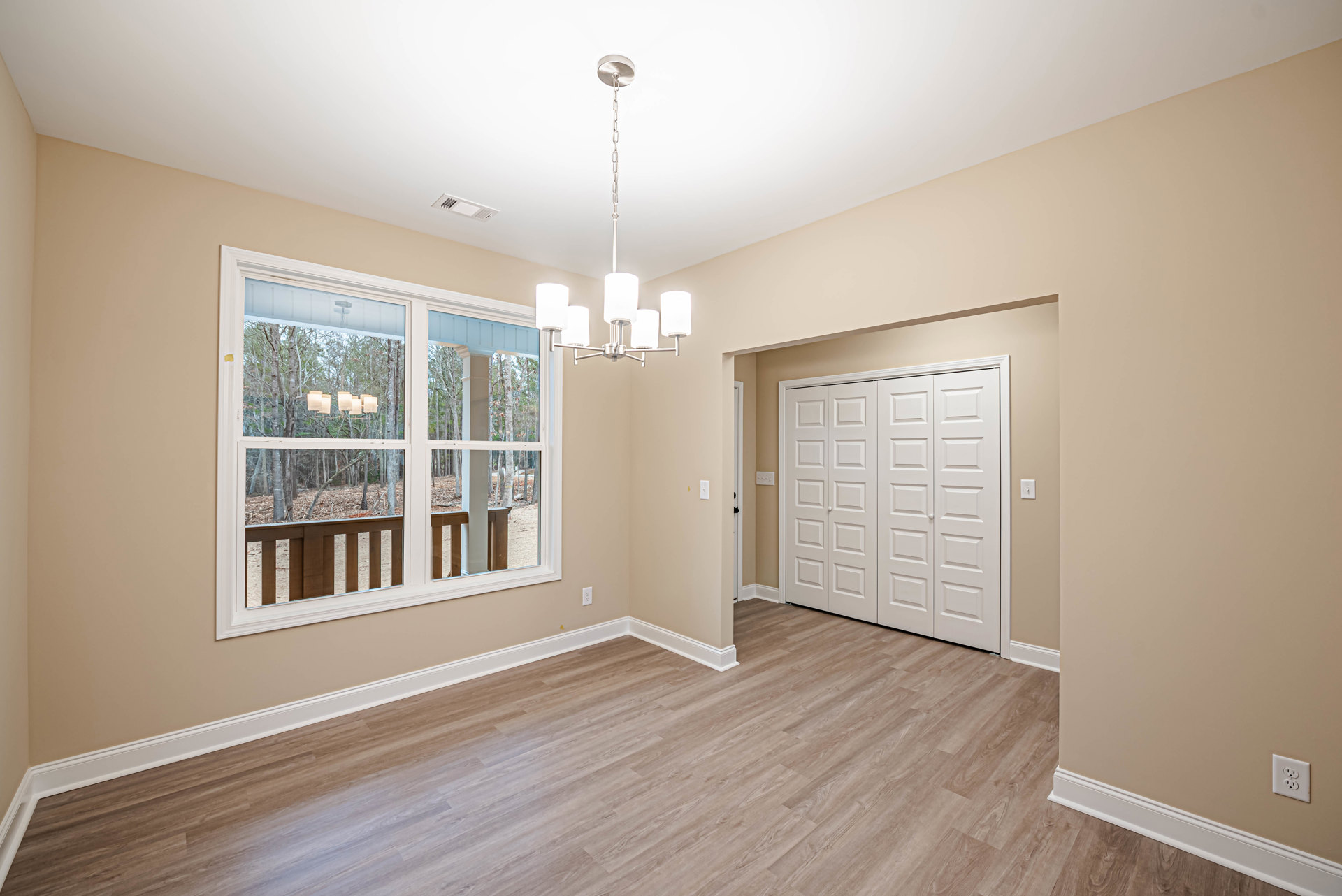 Room with warm wood flooring, white closet doors, large window overlooking trees, modern chandelier, and white door; close-up details include electrical outlet and white lamp
