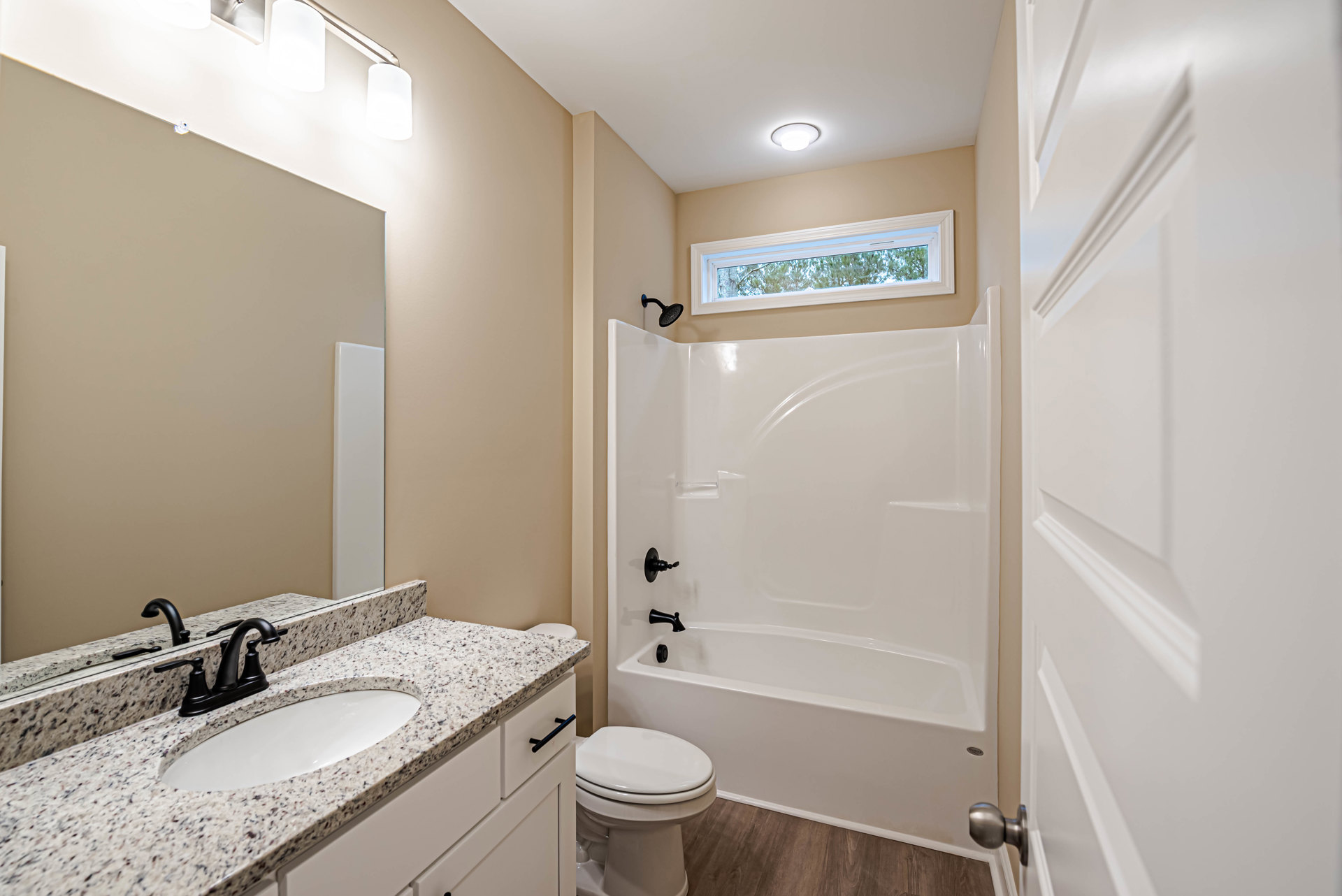 Modern bathroom with white bathtub, closed toilet, rectangular sink featuring a black faucet, tiled walls, and a window overlooking green trees.