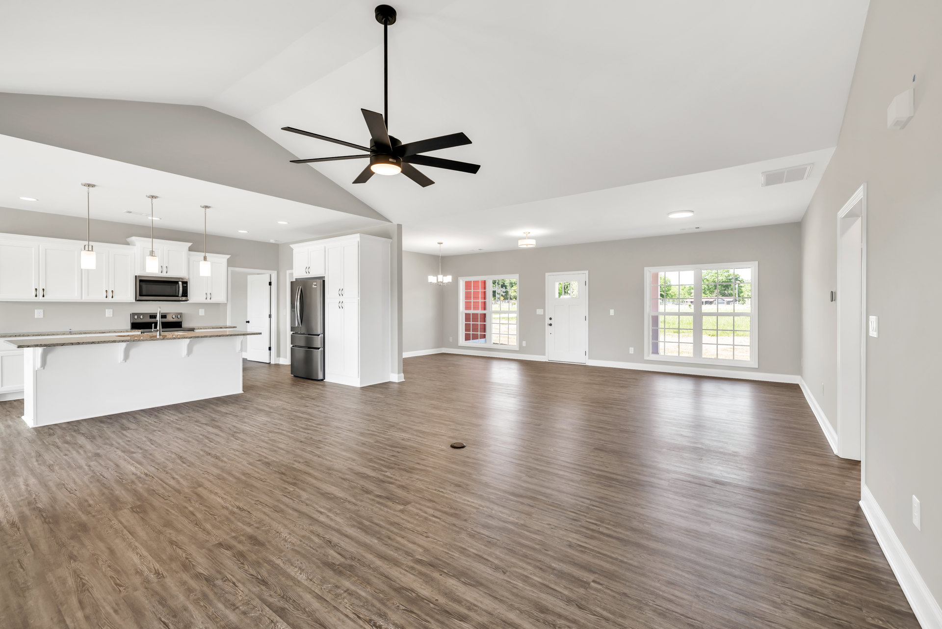 Spacious room with wood flooring, ceiling fan with light fixture, multi-pane window, and neutral walls