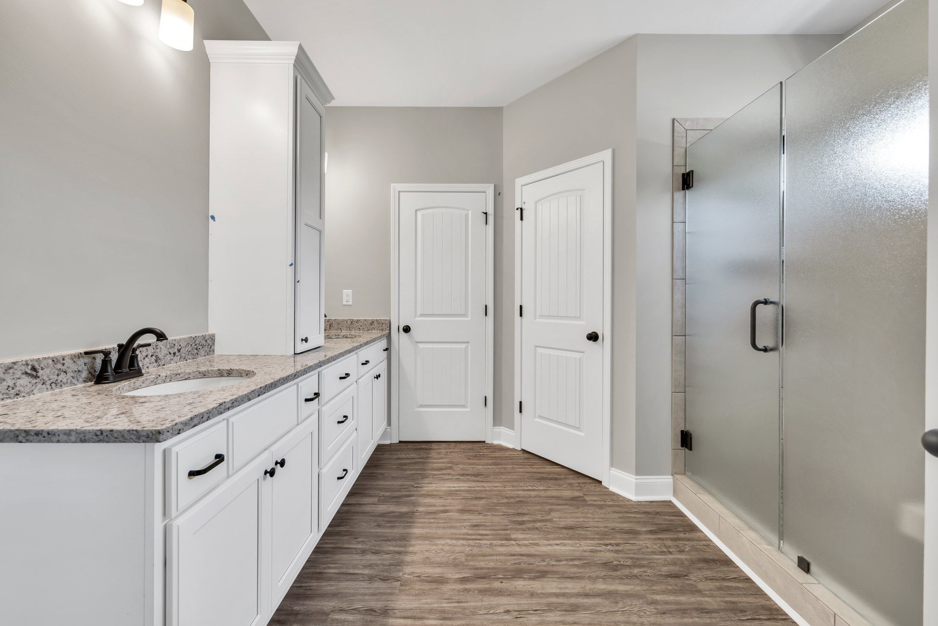 Bathroom with white shaker cabinets, marble countertop, black faucet, glass shower enclosure, white door with black handle, tile flooring