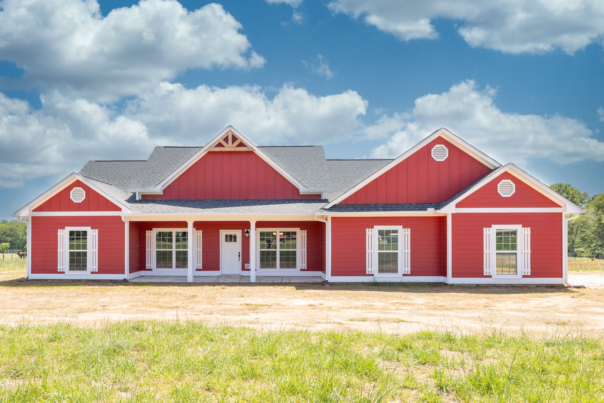 Red house with white trim and windows, green lawn in front, blue sky with scattered clouds overhead