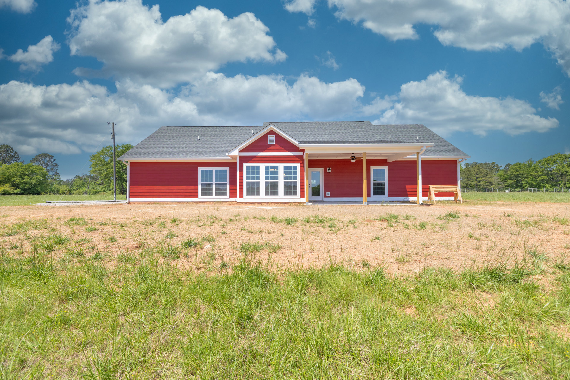 Red house with white trim and roof, expansive green grass field in front, rural landscape with trees and cloudy sky in background